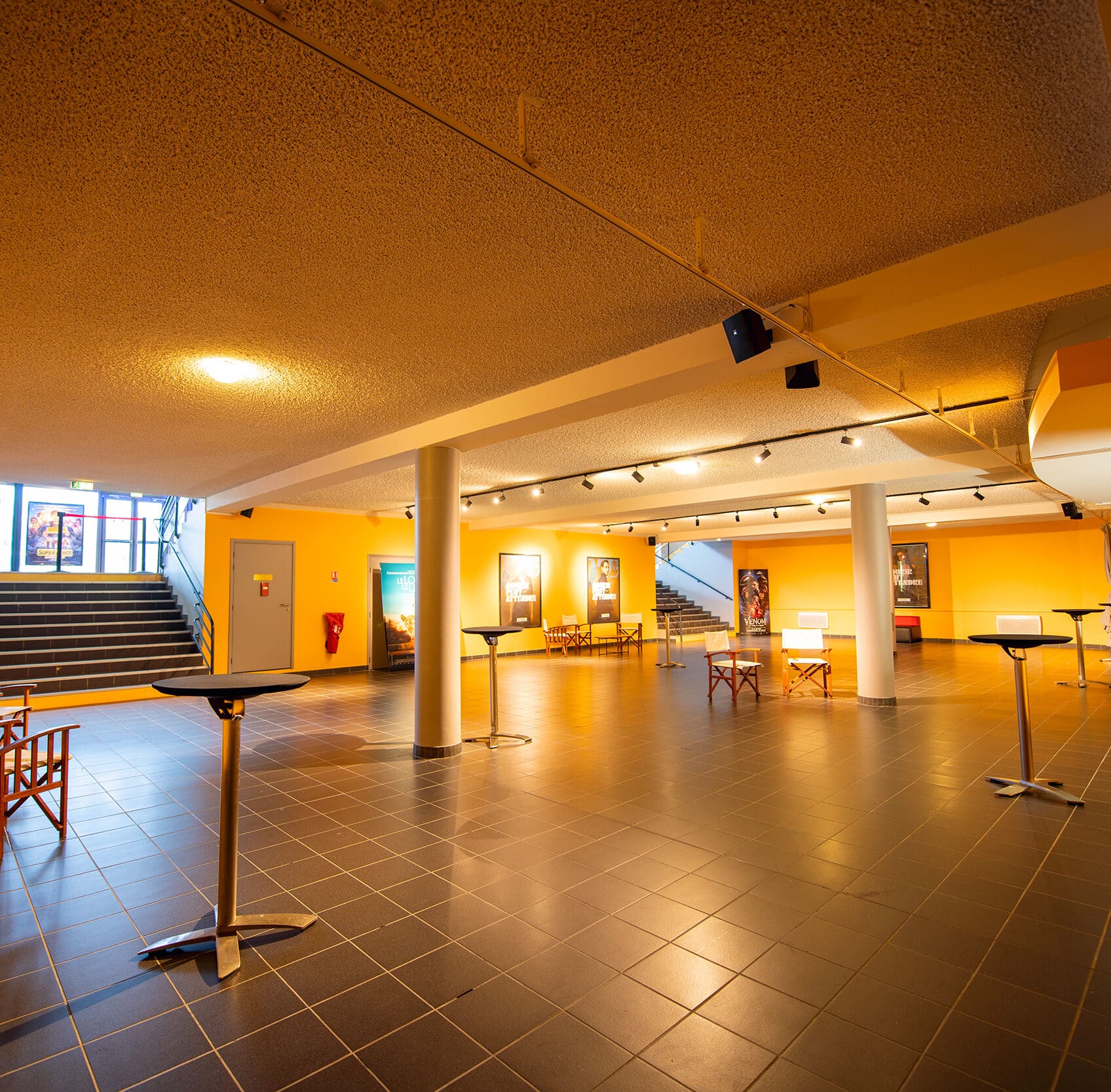 Espace cocktail du cinéma éclairé par des lumières chaudes créant une ambiance chaleureuse, équipé d'un mobilier de réception.