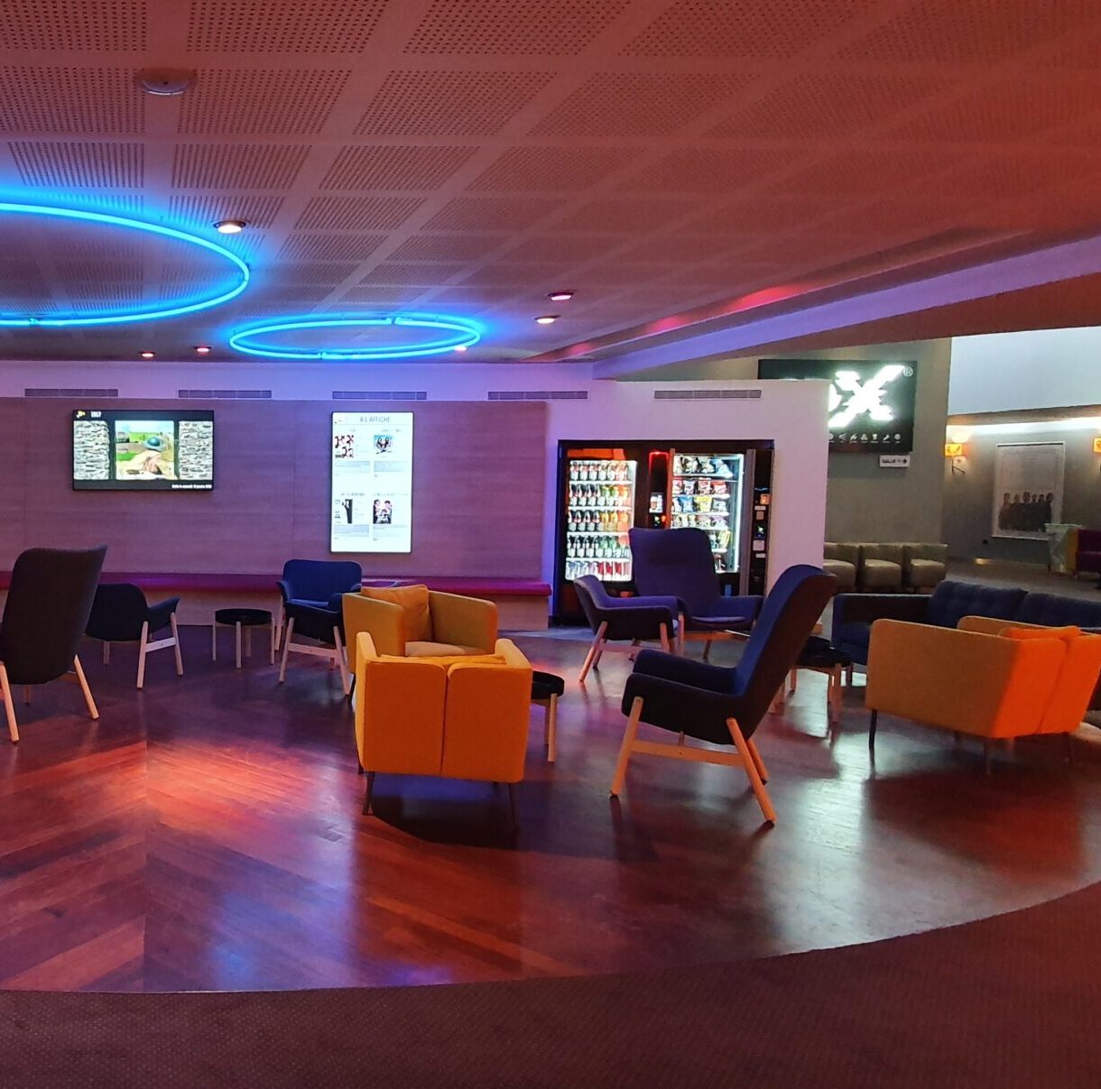 Espace de réception du cinéma avec fauteuils colorés, éclairage LED bleu et distributeurs automatiques.