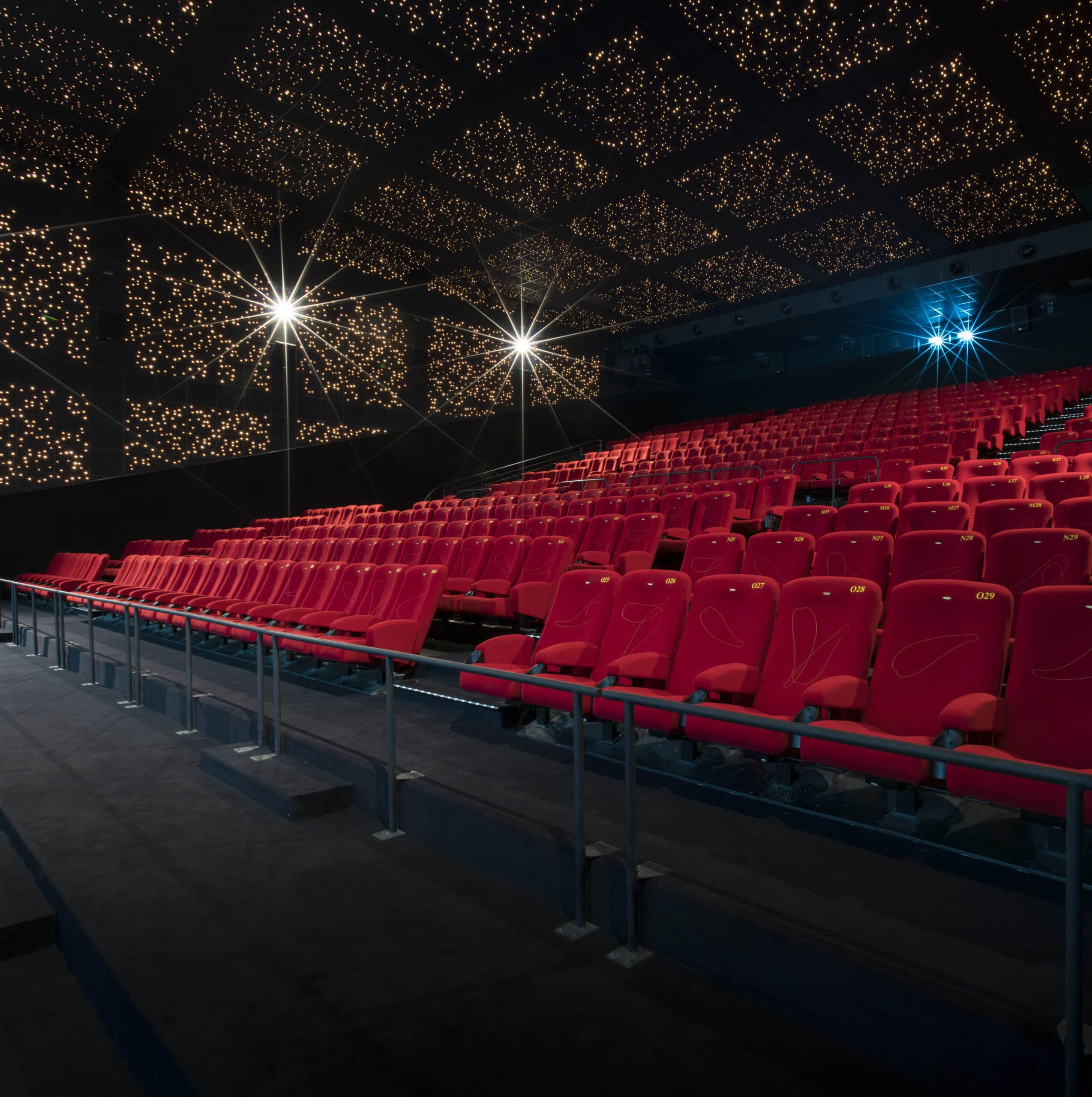 Vue latérale de la salle de cinéma montrant les fauteuils en velours rouges et l’agencement des rangées.