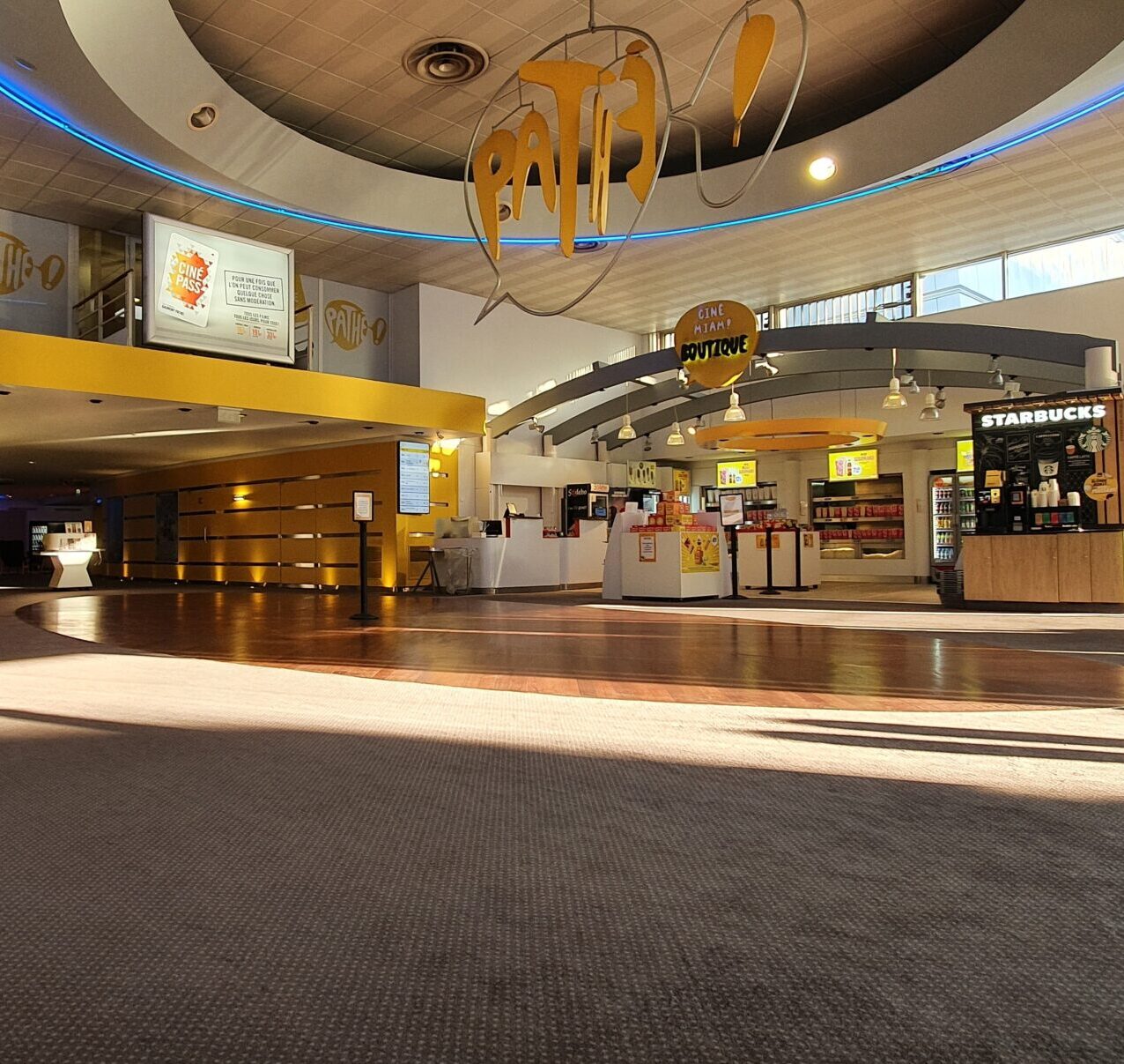 Hall principal du cinéma Pathé avec boutiques, comptoirs lumineux et enseigne Starbucks sous un design moderne.