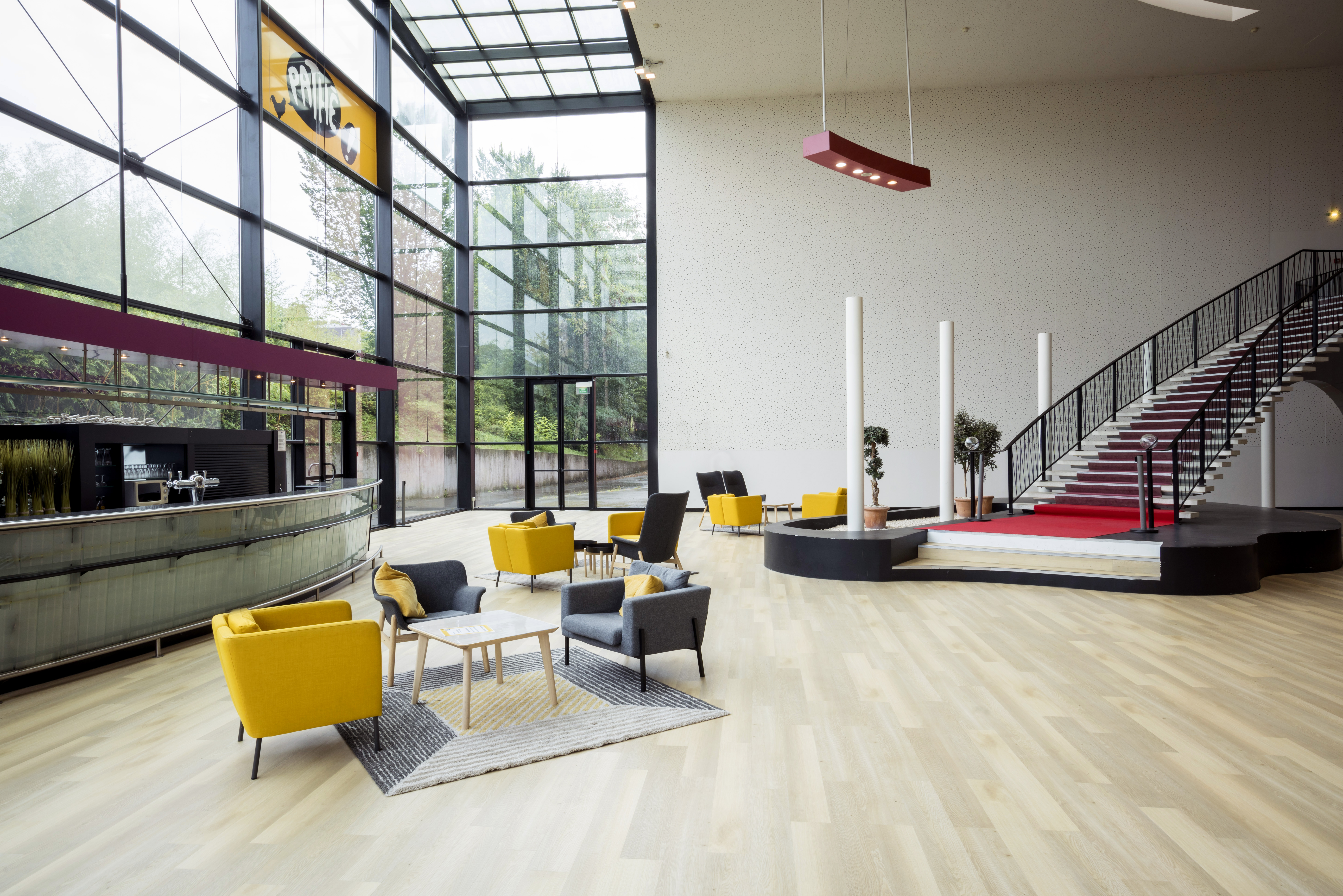 Hall d'entrée lumineux du cinéma Pathé avec une grande baie vitrée, des sièges colorés, une décoration végétale et un comptoir moderne.