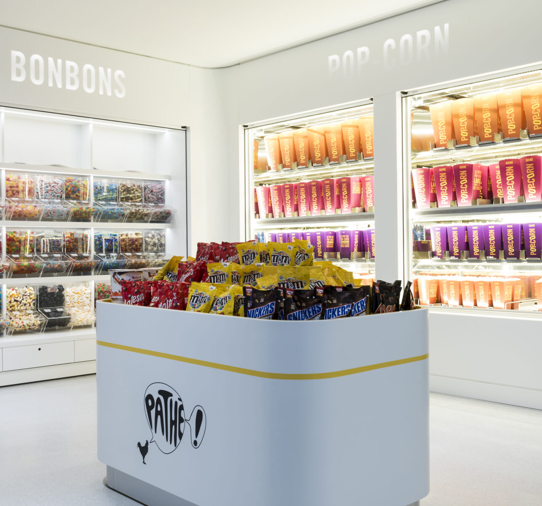 Espace confiserie du cinéma Pathé avec comptoir de pop-corn, distributeurs de boissons en libre-service et îlots de snacks et confiseries.