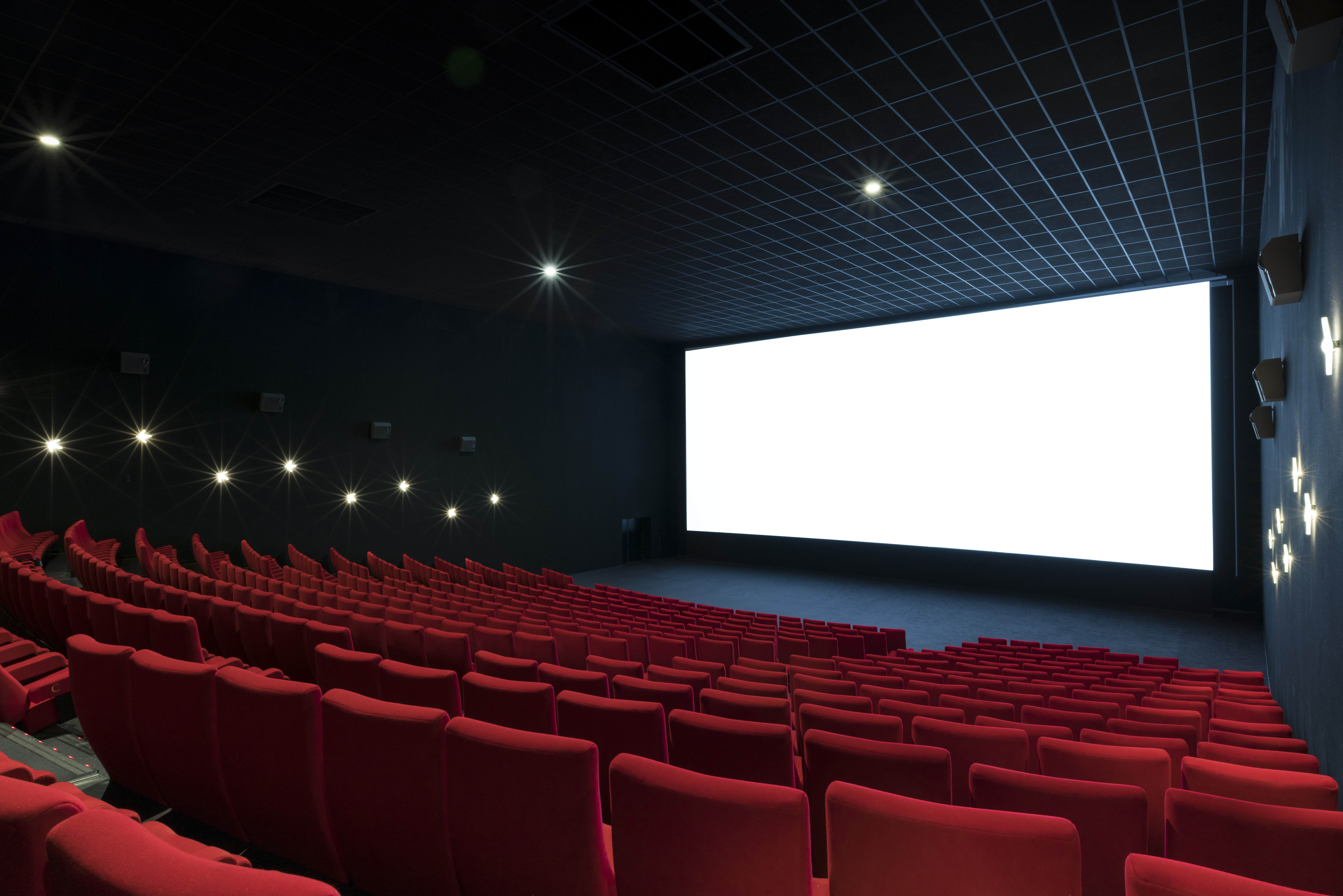 Vue depuis l’arrière d'une salle du cinéma Pathé avec ses rangées de fauteuils en velours rouges orientés vers l’écran.