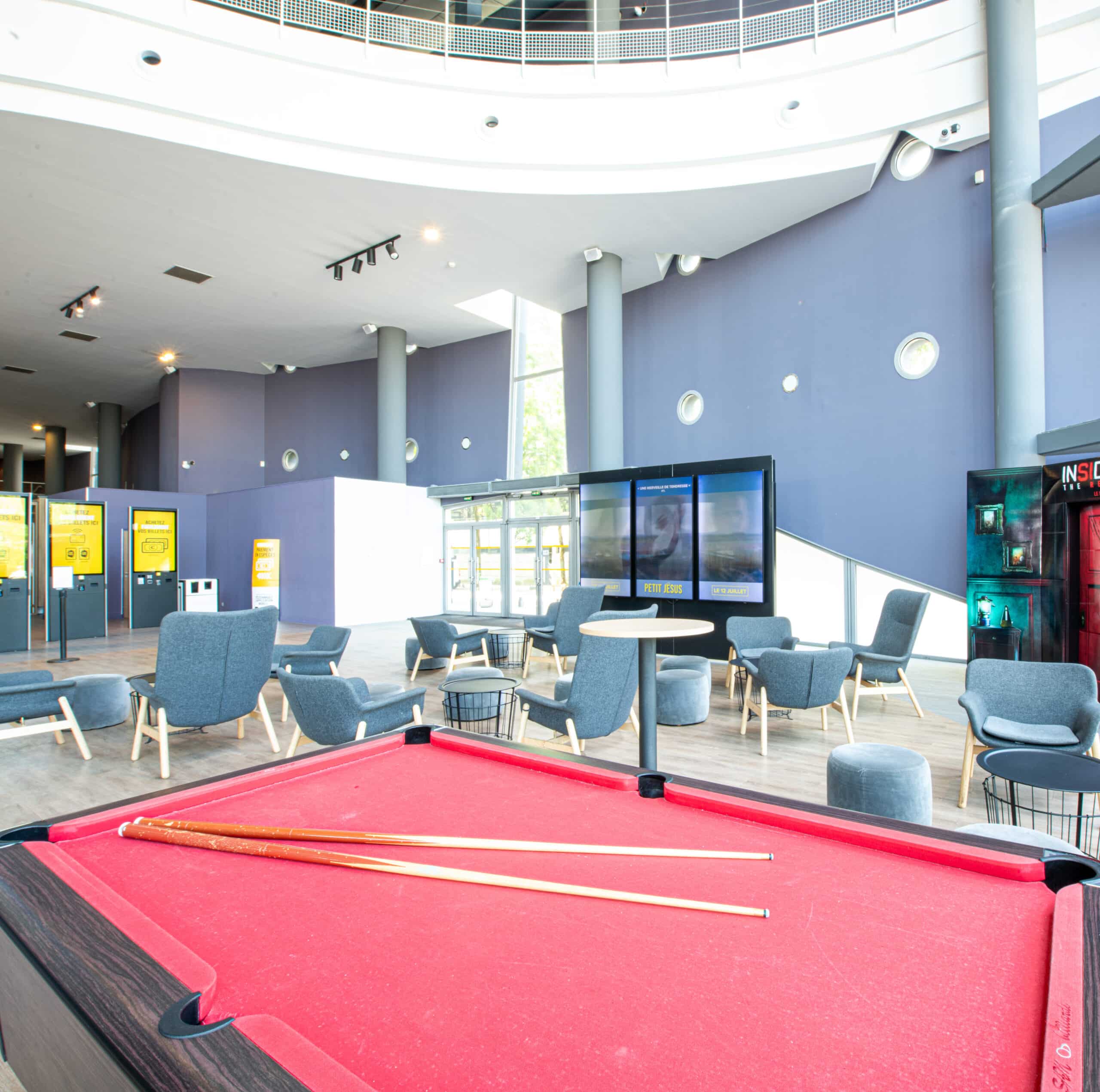 Espace cocktail du cinéma à la lumière du jour grâce à ses grandes baies vitrées, équipé d'un mobilier de réception. et d'un espace de jeu avec un billard.
