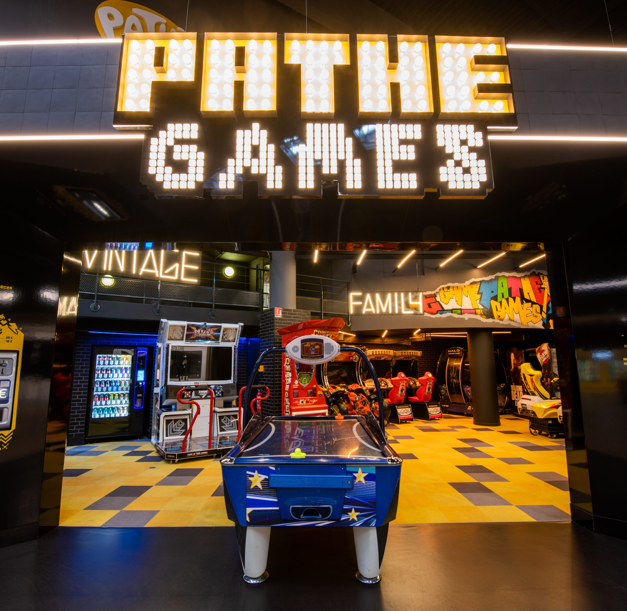 Espace Pathé Games avec différentes machines d’arcade et de jeux vidéo, éclairage néon coloré, ambiance moderne et ludique, proposant des jeux pour tous les âges dans un cadre convivial.
