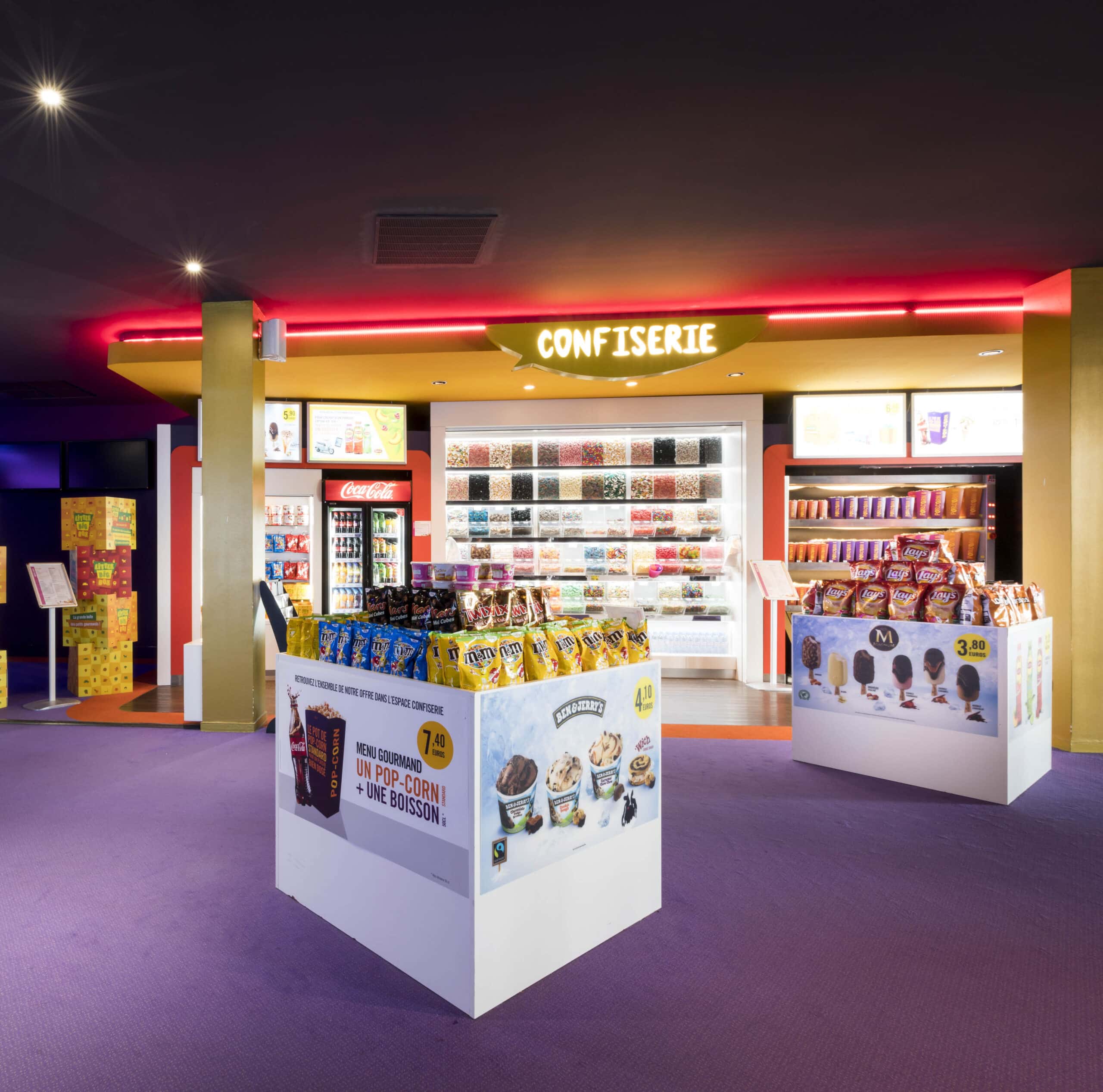 Espace confiserie du cinéma Pathé avec comptoir de pop-corn, distributeurs de boissons en libre-service et îlots de snacks et confiseries.