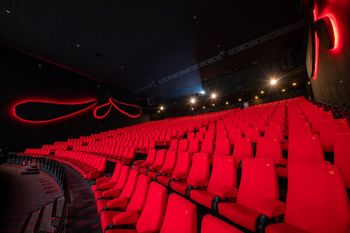 Vue latérale de la salle de cinéma montrant les fauteuils en velours rouges et l’agencement des rangées.