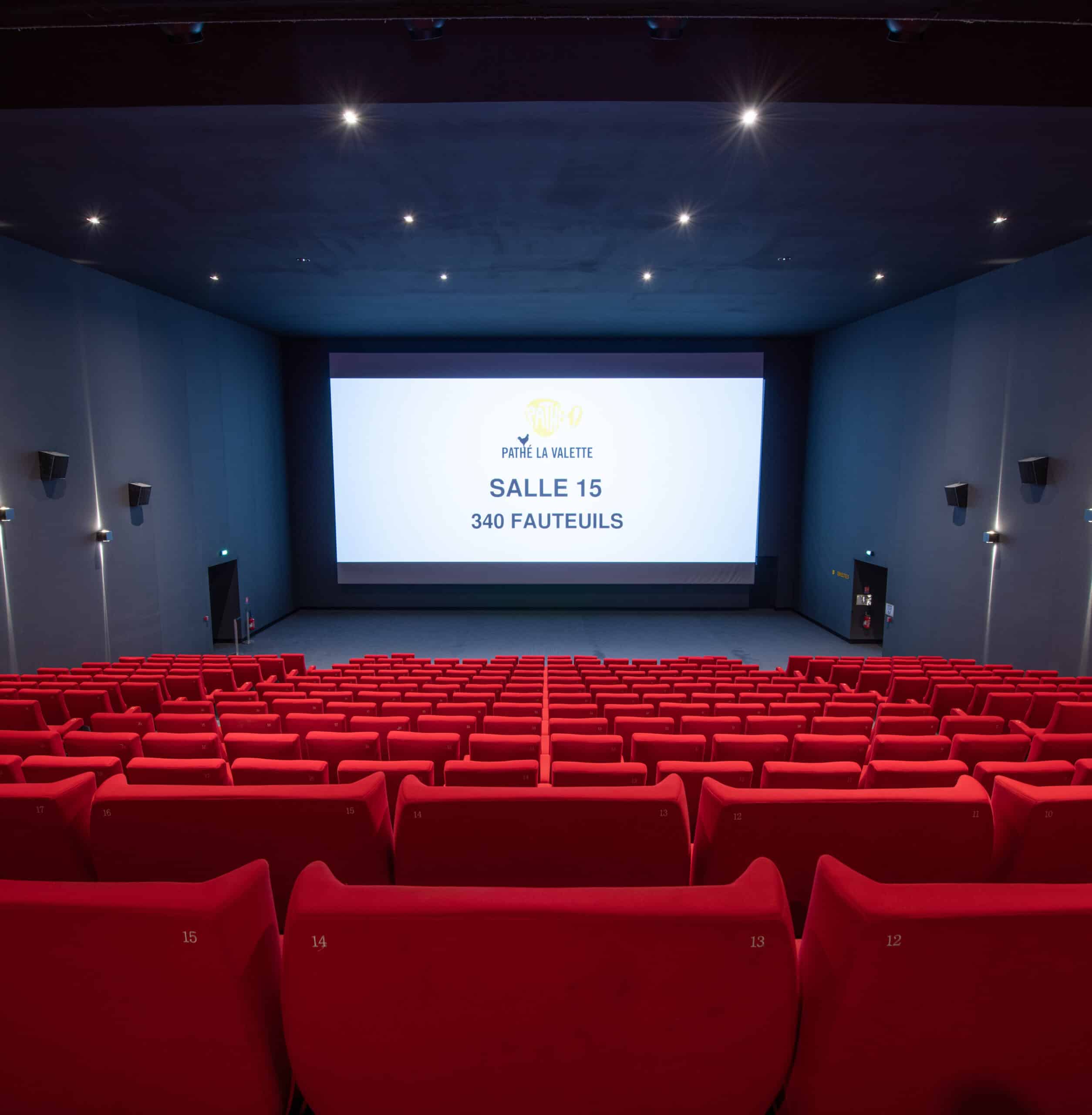 Vue depuis l’arrière de la salle 15 du cinéma Pathé La Valette avec rangées de fauteuils en velours rouges orientés vers l’écran.