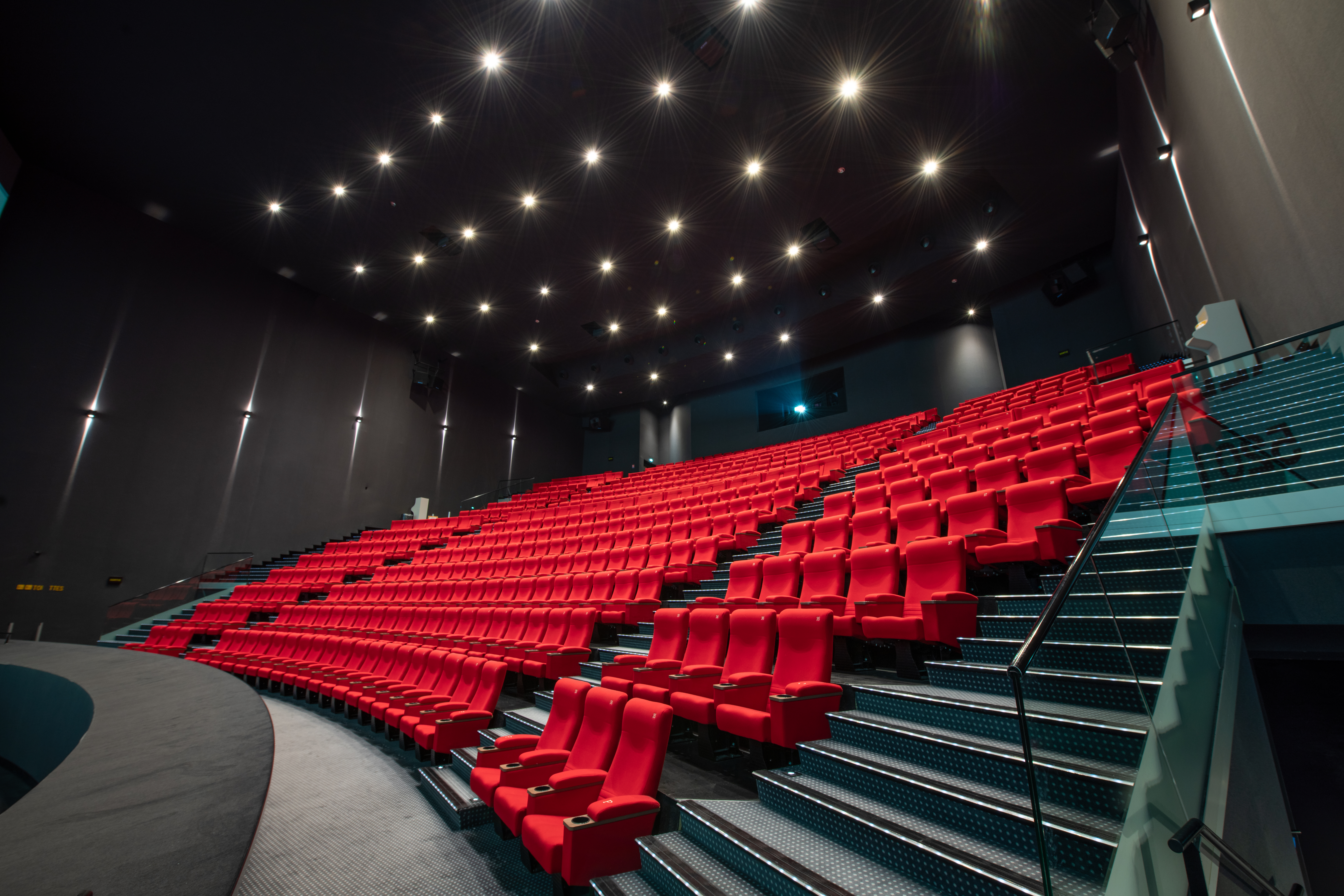 Vue latérale de la salle de cinéma montrant les fauteuils en velours rouges et l’agencement des rangées ainsi que son espace scénique.