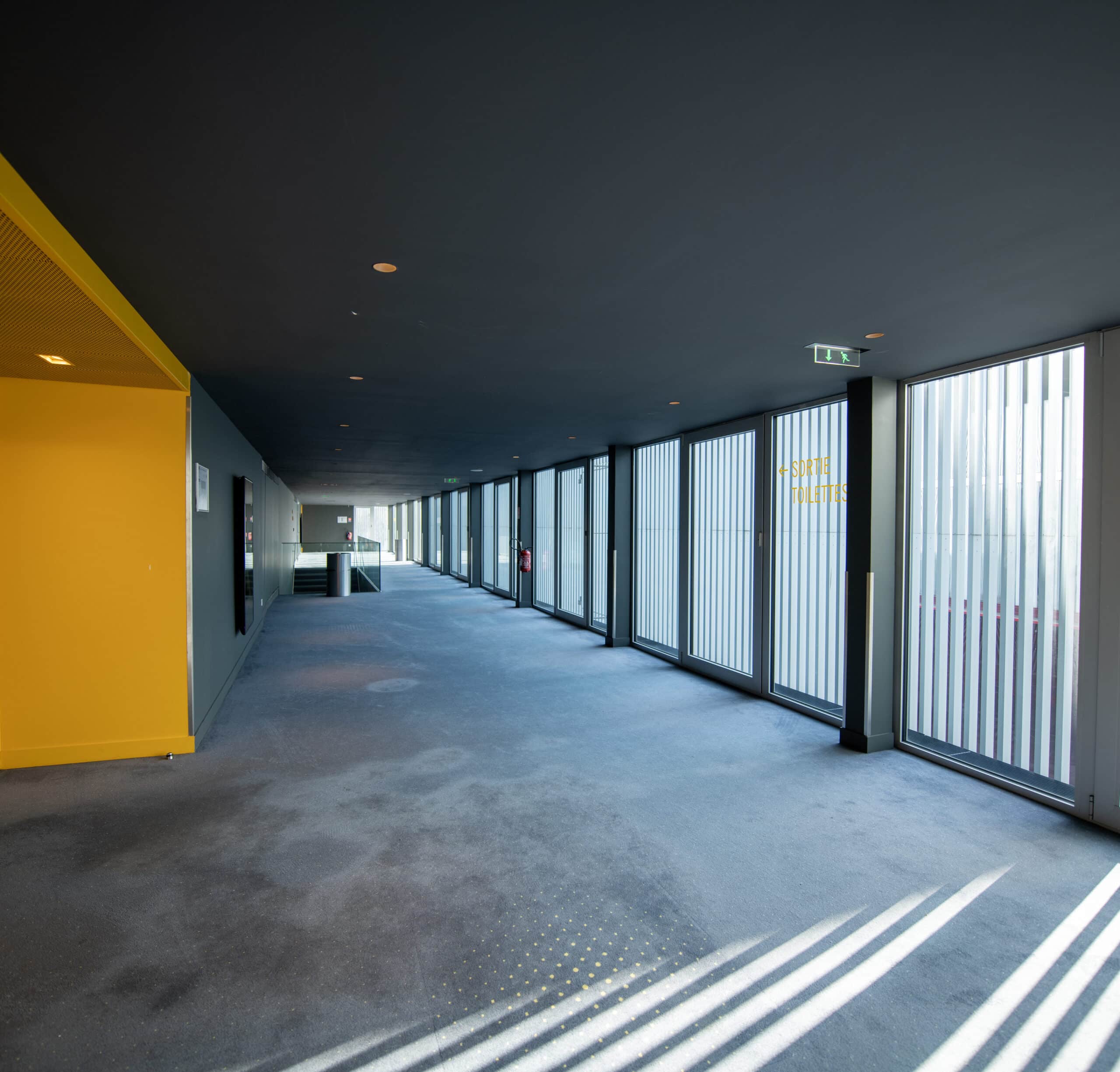Couloir lumineux avec de grandes fenêtres verticales, une porte numérotée 