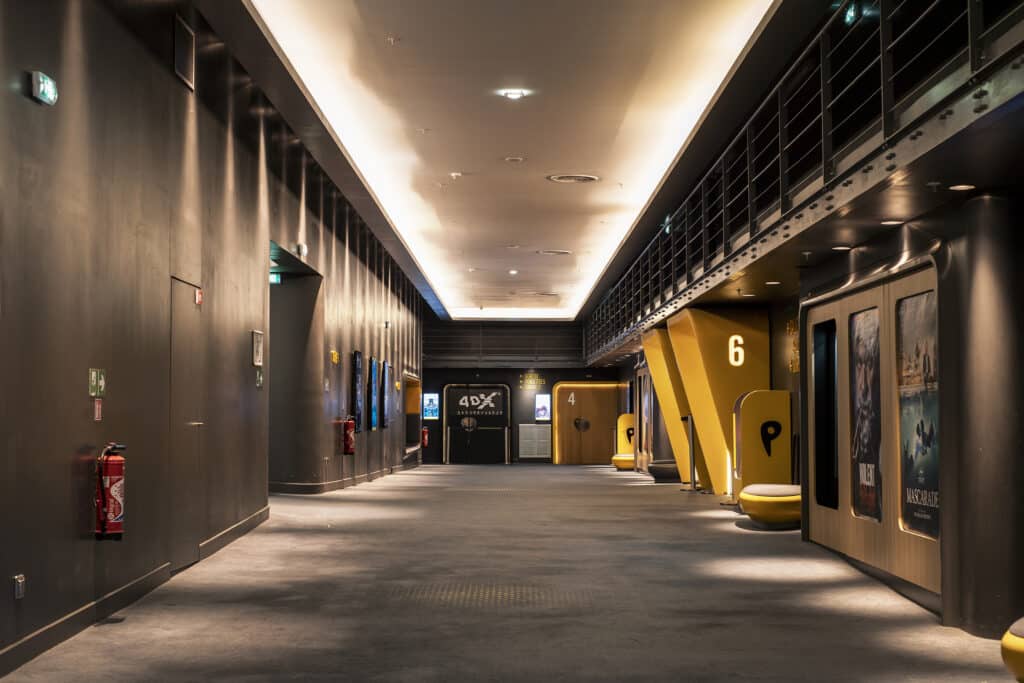 Couloir spacieux menant aux salles de cinéma, avec numéros bien visibles, affiches de films et éclairage tamisé