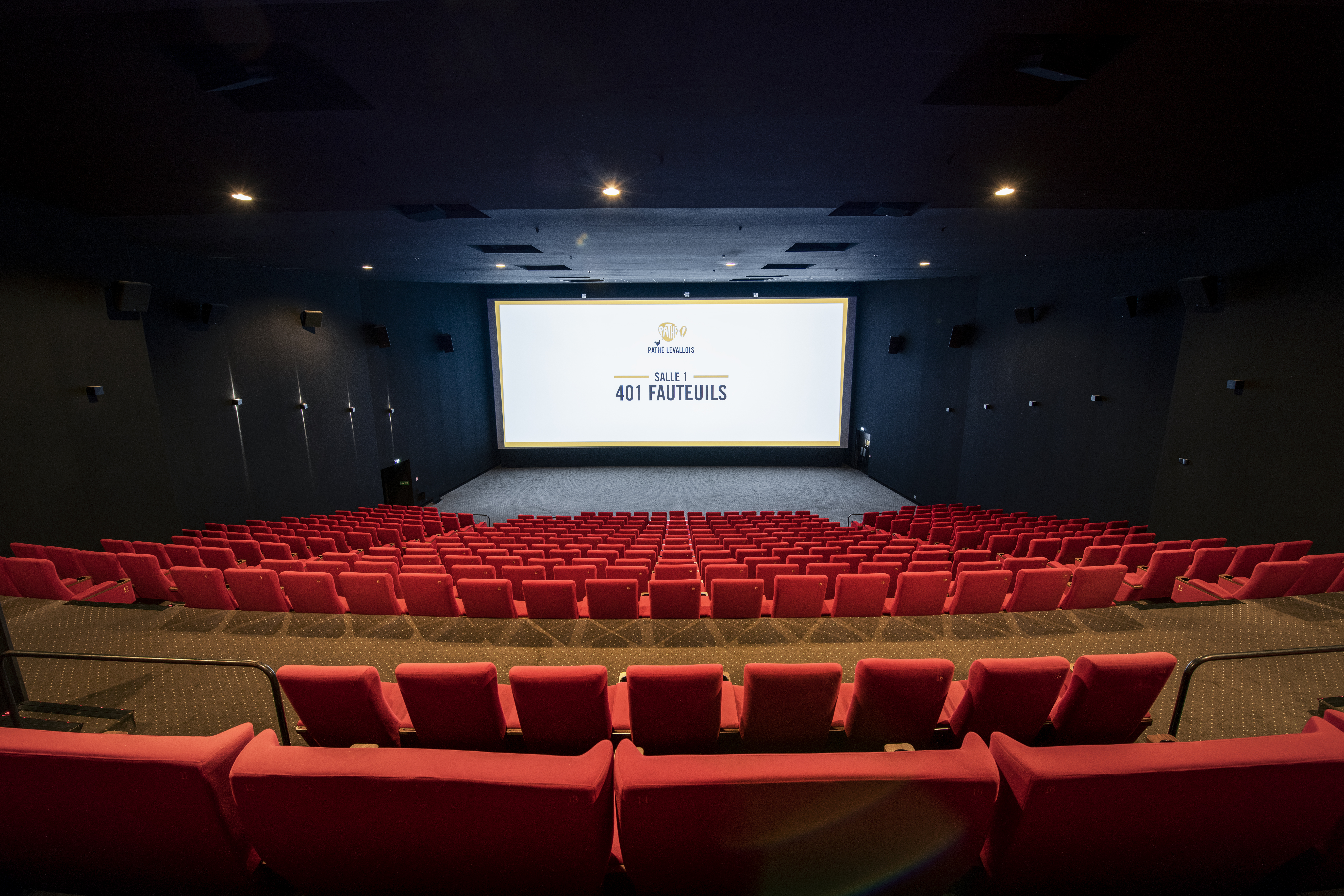 Vue depuis l’arrière de la salle 1 du cinéma Pathé Levallois avec ses rangées de fauteuils en velours rouges orientés vers l’écran.