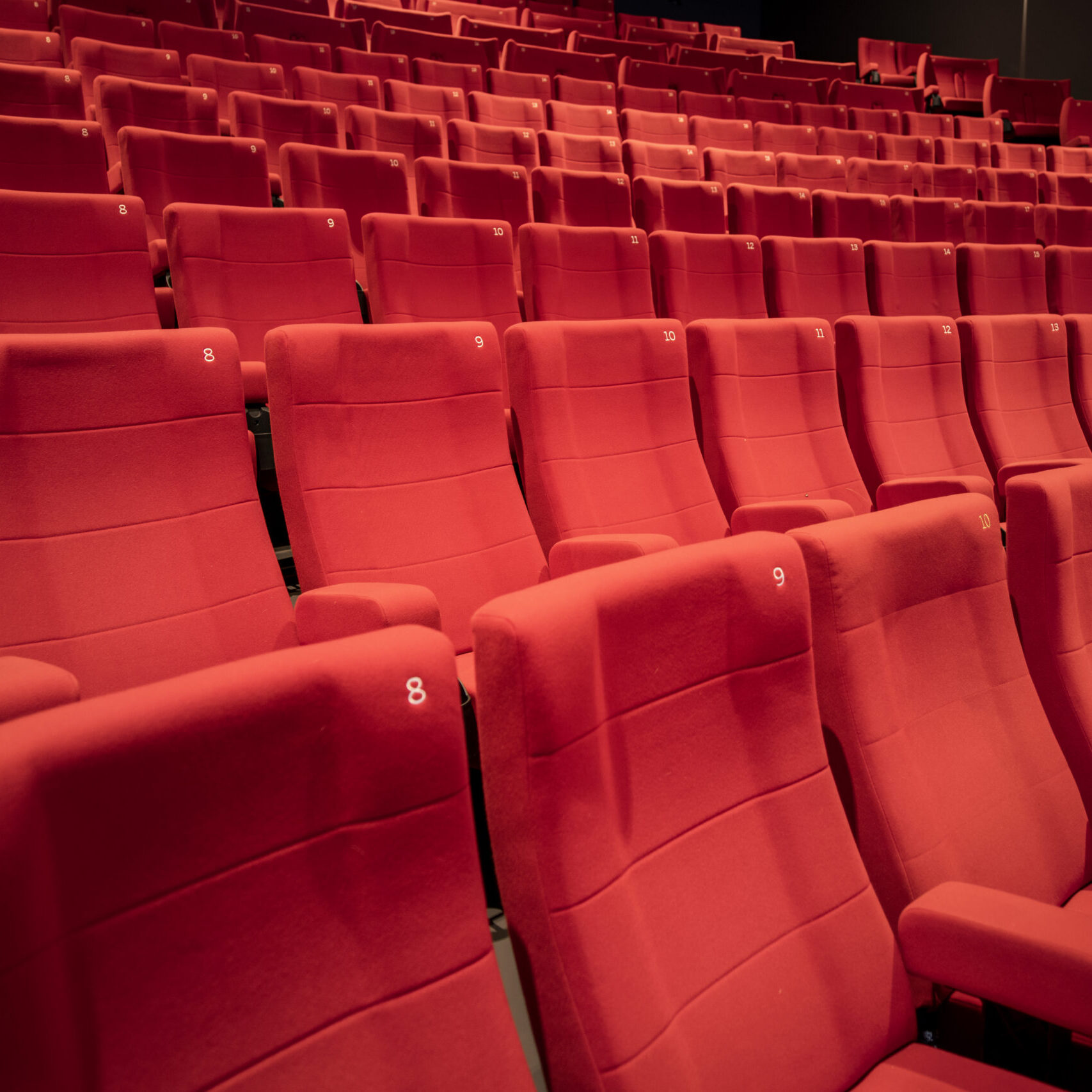 Rangées de fauteuils de cinéma en tissu rouge vif. Chaque siège est numéroté pour faciliter le repérage des places.