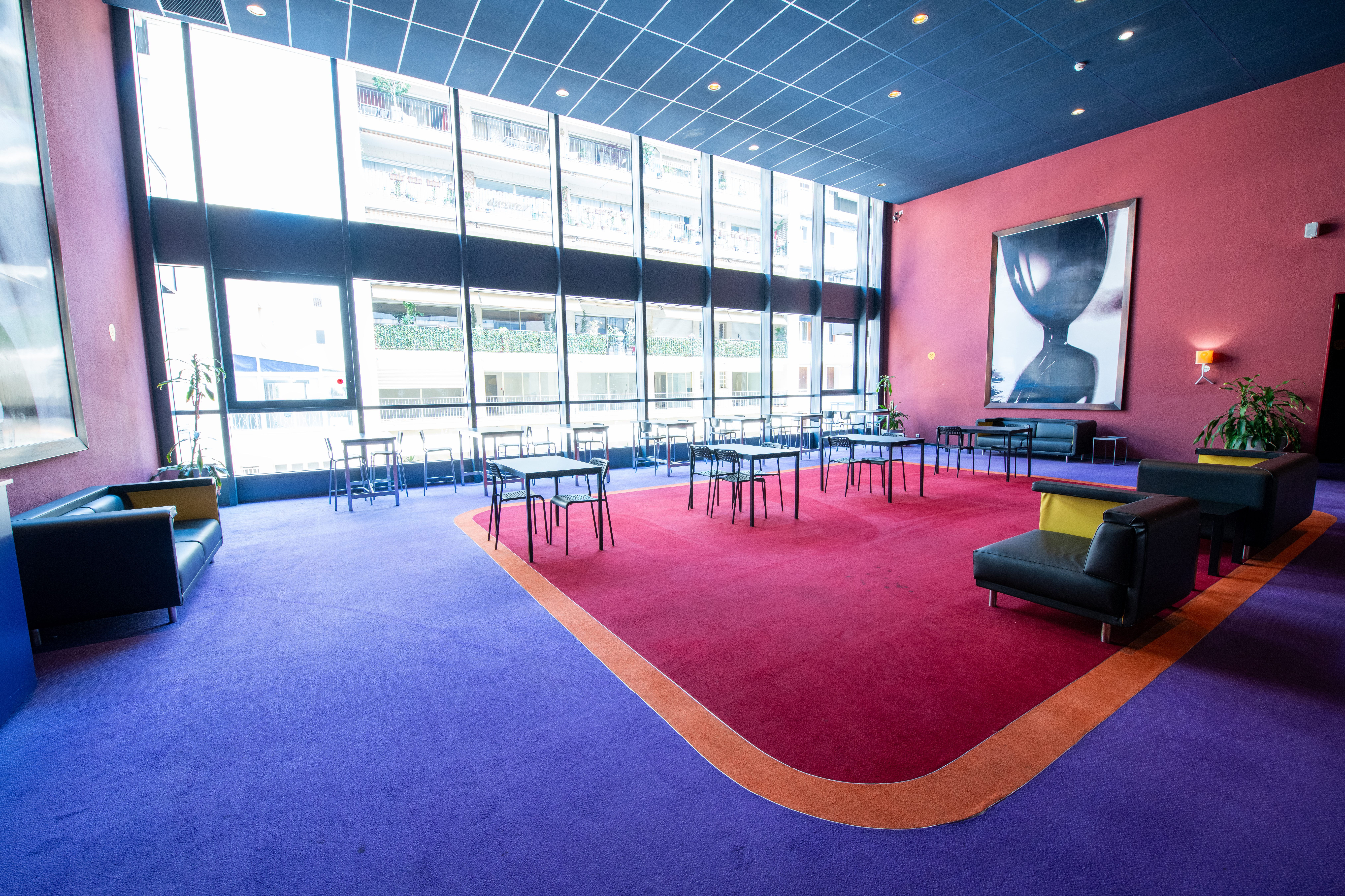 Espace cocktail du cinéma à la lumière du jour grâce à ses grandes baies vitrées, équipé d'un mobilier de réception et de salon.