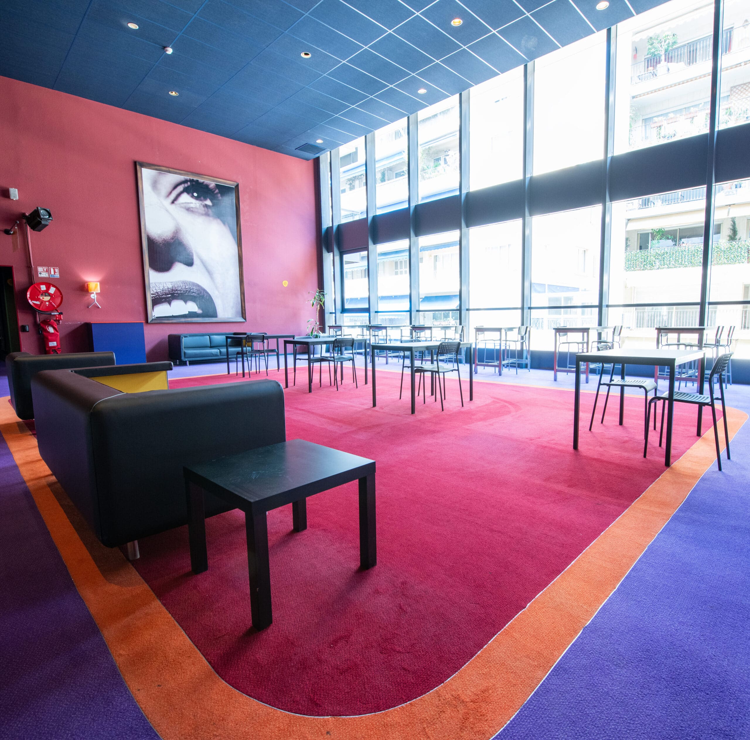 Espace cocktail du cinéma à la lumière du jour grâce à ses grandes baies vitrées, équipé d'un mobilier de réception et de salon.
