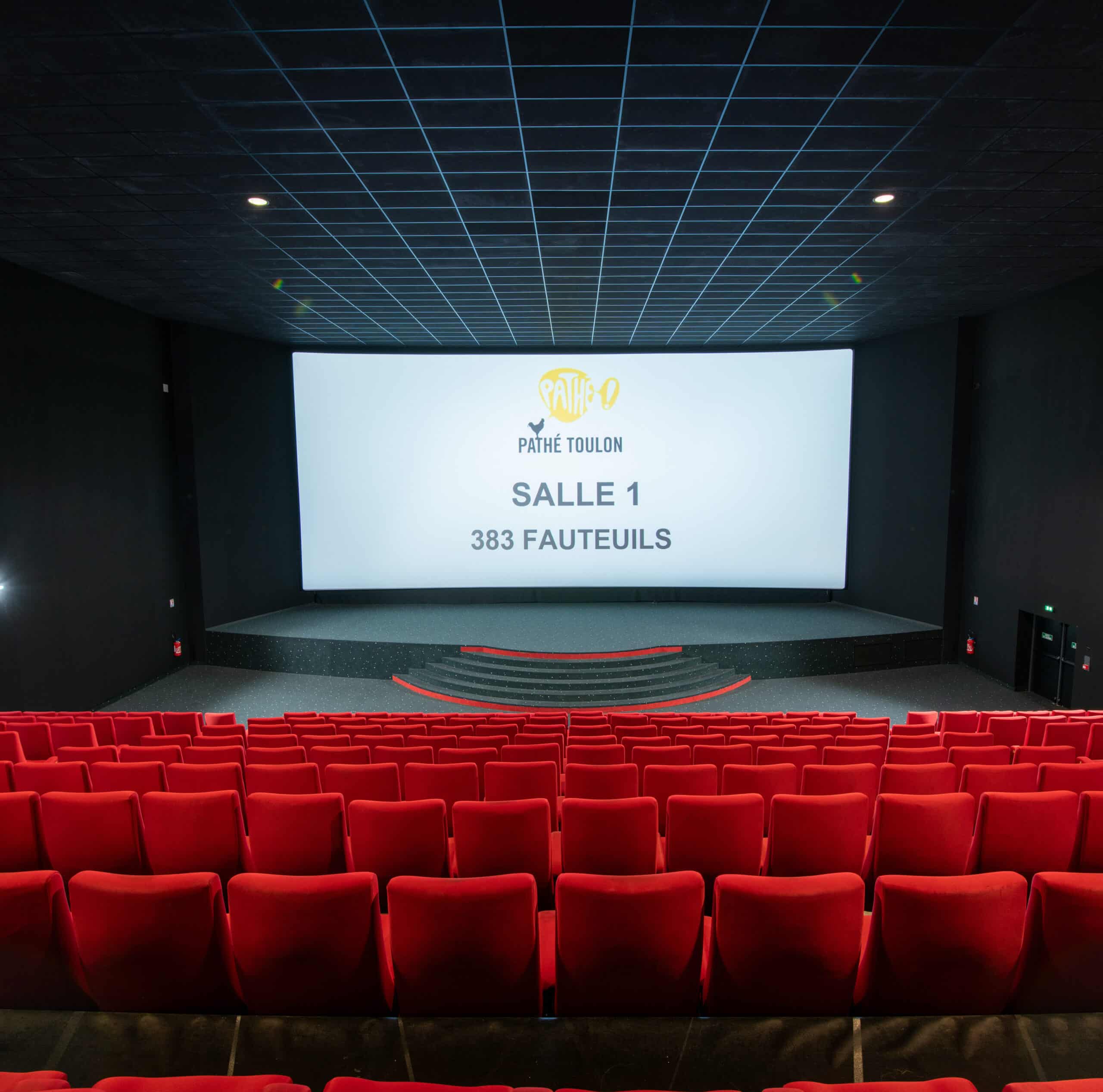 Vue depuis l’arrière de la salle 1 du cinéma Pathé Toulon avec rangées de fauteuils en velours rouges orientés vers l’écran.