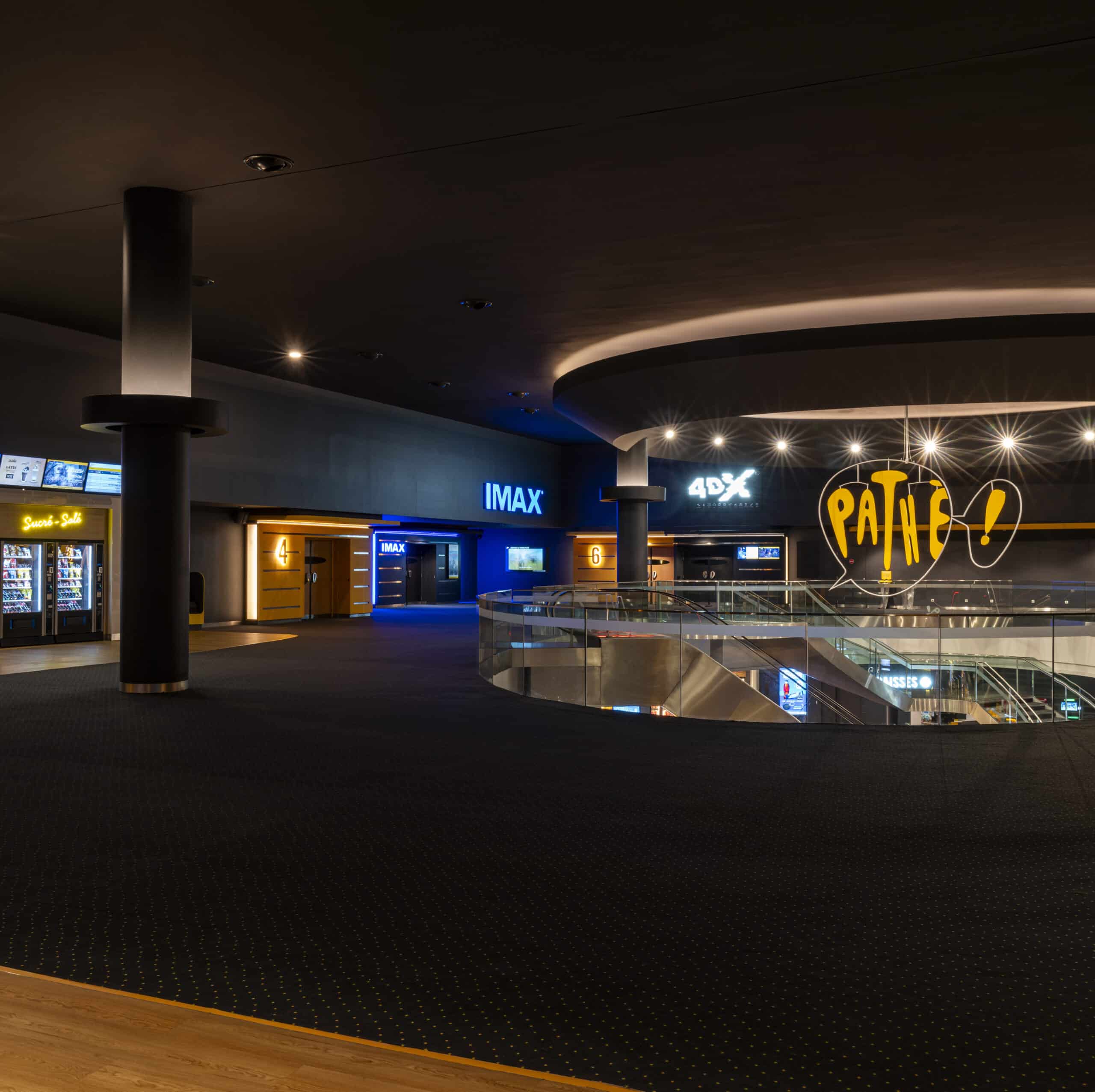 Grand espace de réception vide situé au premier étage du cinéma éclairé par des néons chaleureux.