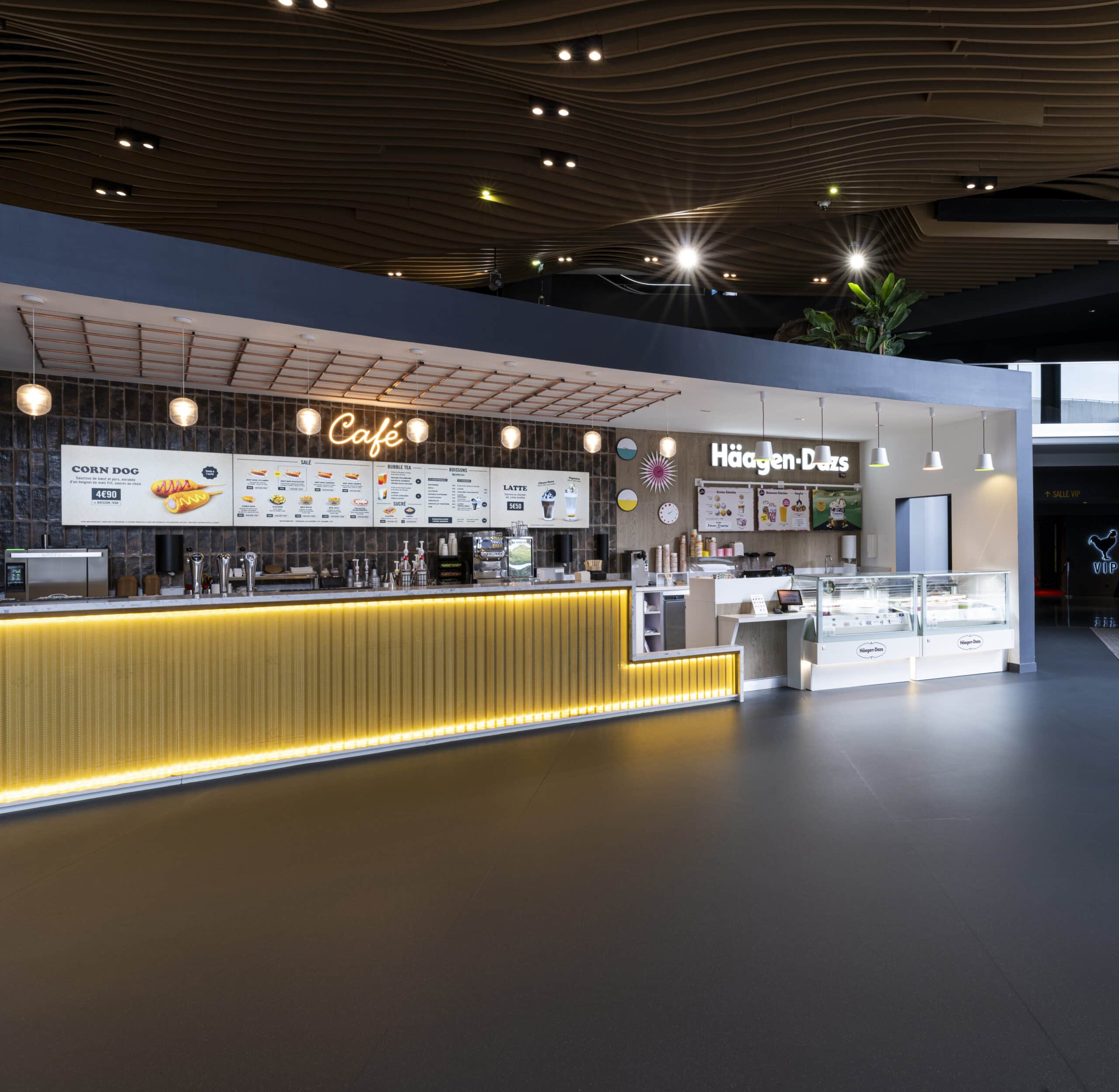 Espace café et Häagen-Dazs dans le cinéma Pathé, avec comptoir lumineux, enseignes et plafond ondulé moderne.