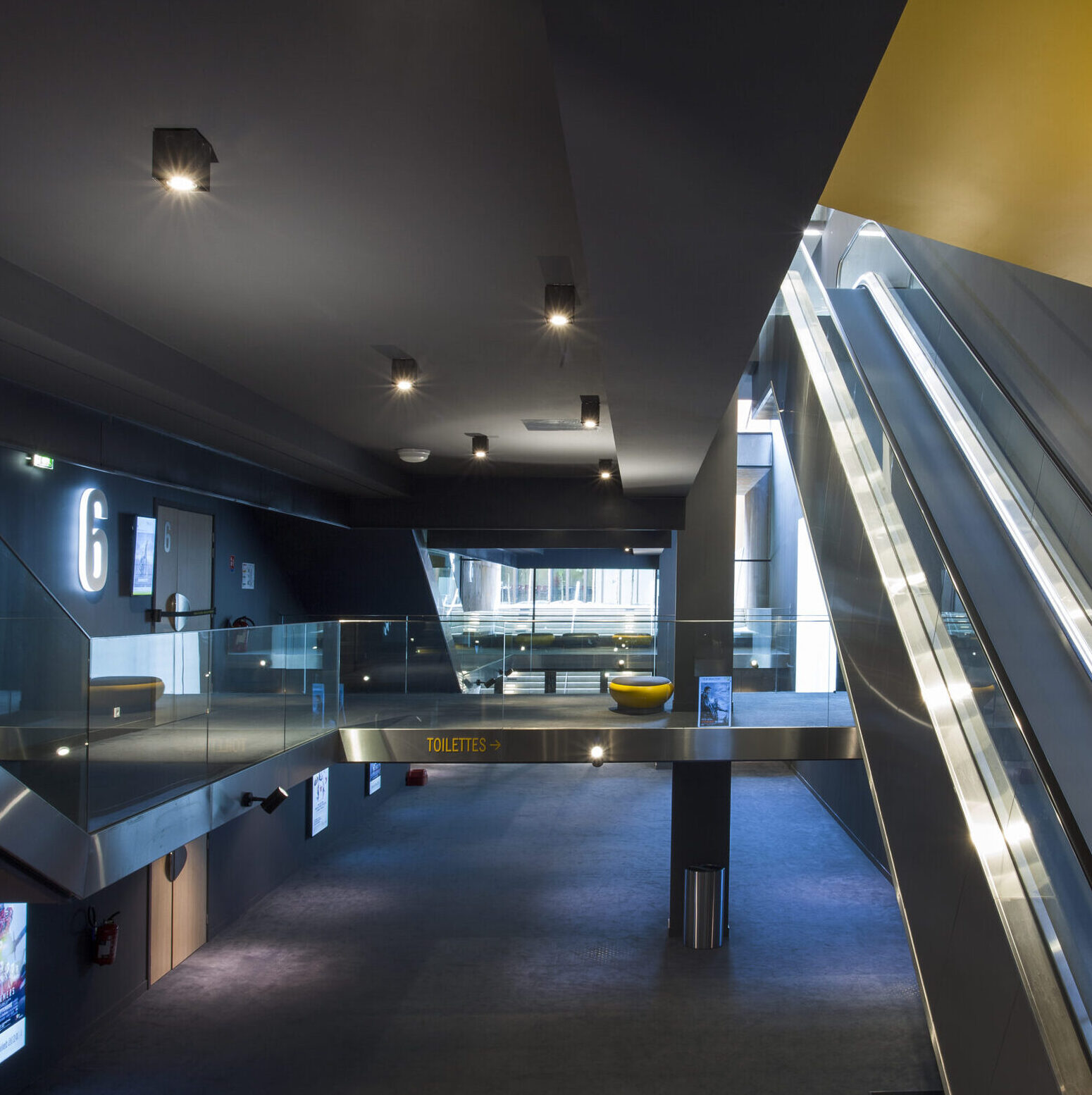 Espace circulatoire du cinéma avec escalators, signalétique moderne et éclairage tamisé.