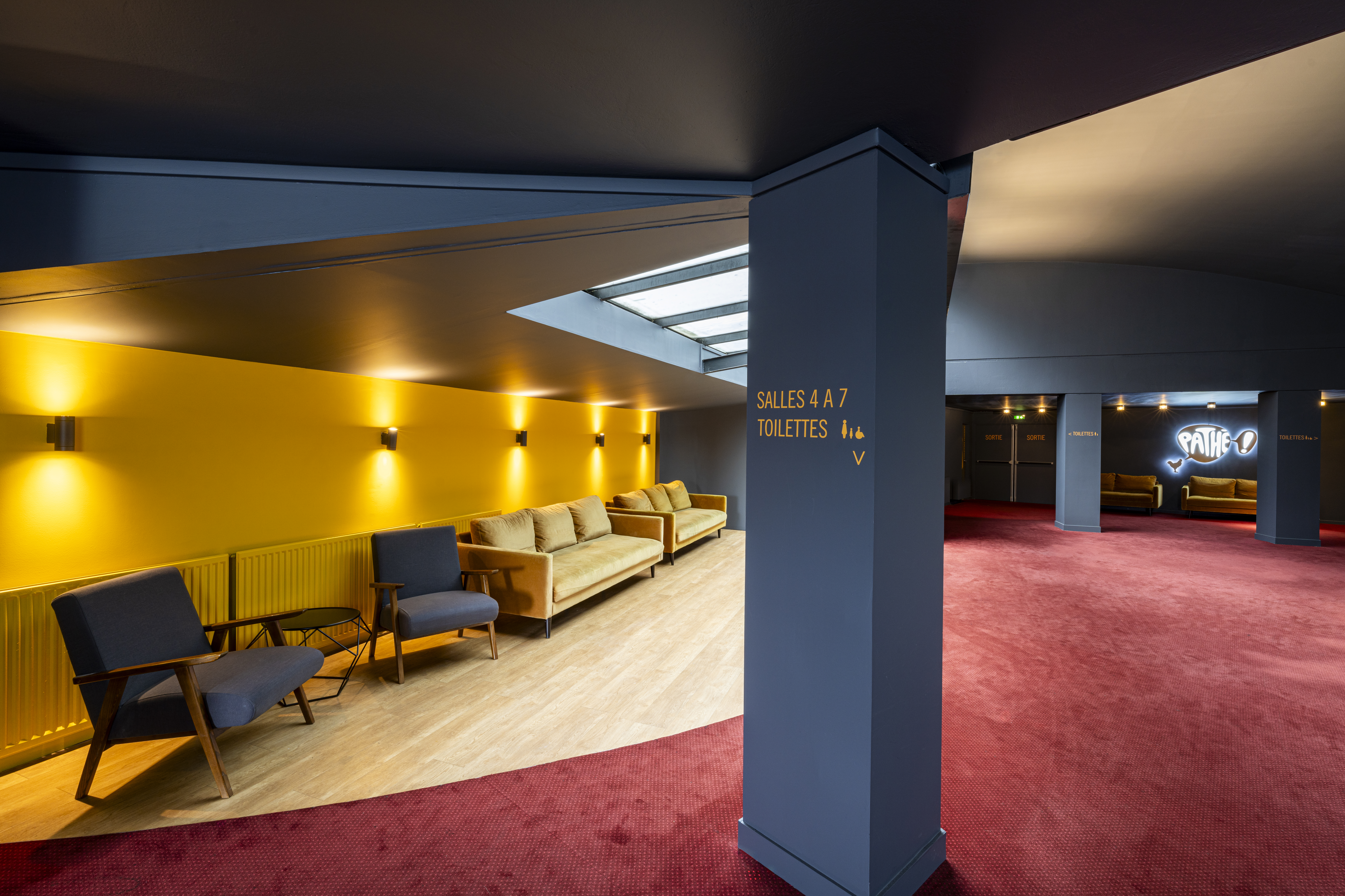 Espace de réception situé dans le hall du cinéma, éclairé par une lumière tamisée et par la lumière naturelle des baies vitrées, avec des canapés et du mobilier de salon.
