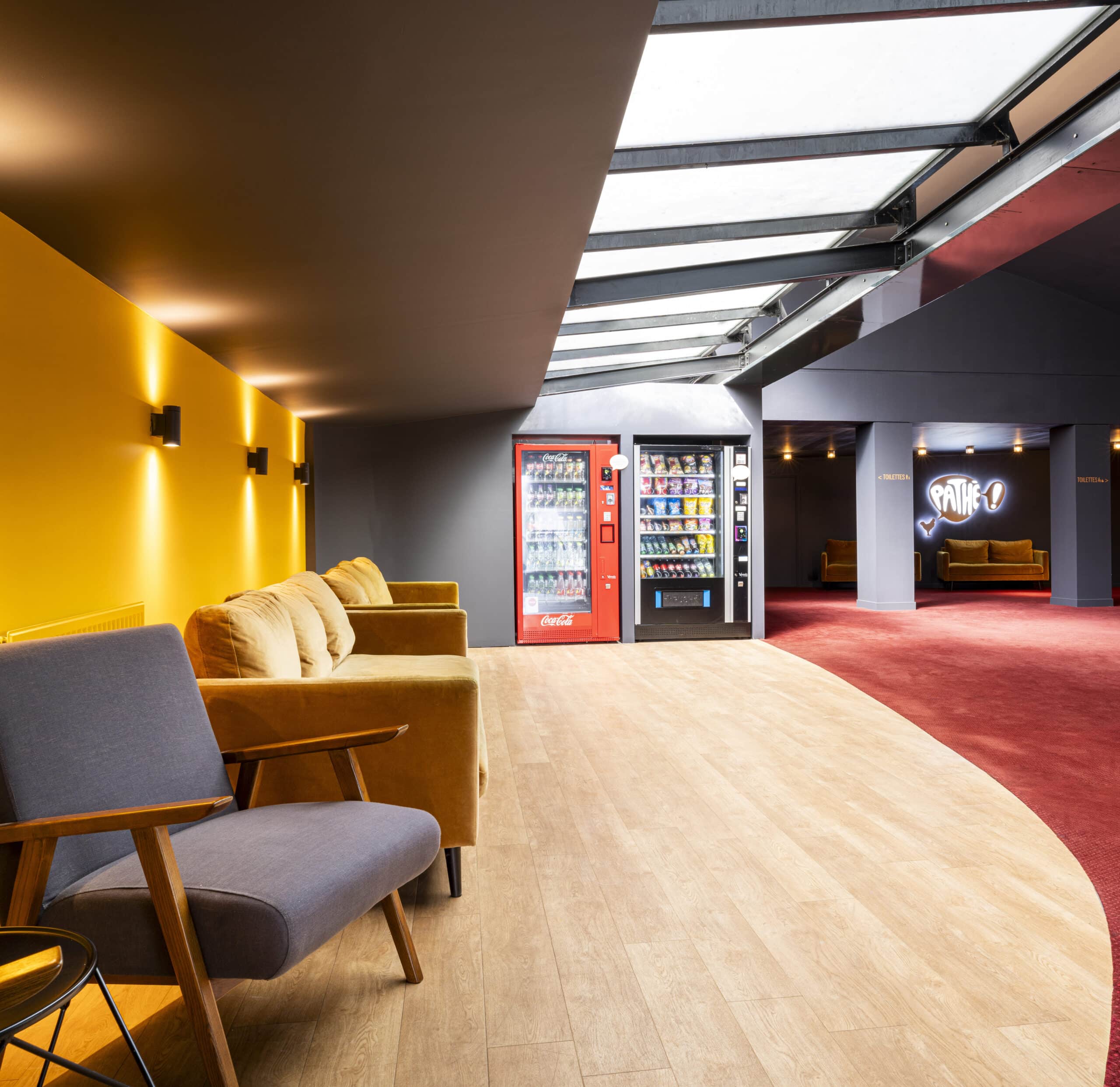 Espace de réception situé dans le hall du cinéma, éclairé par une lumière tamisée et par la lumière naturelle des baies vitrées, avec des canapés et du mobilier de salon.