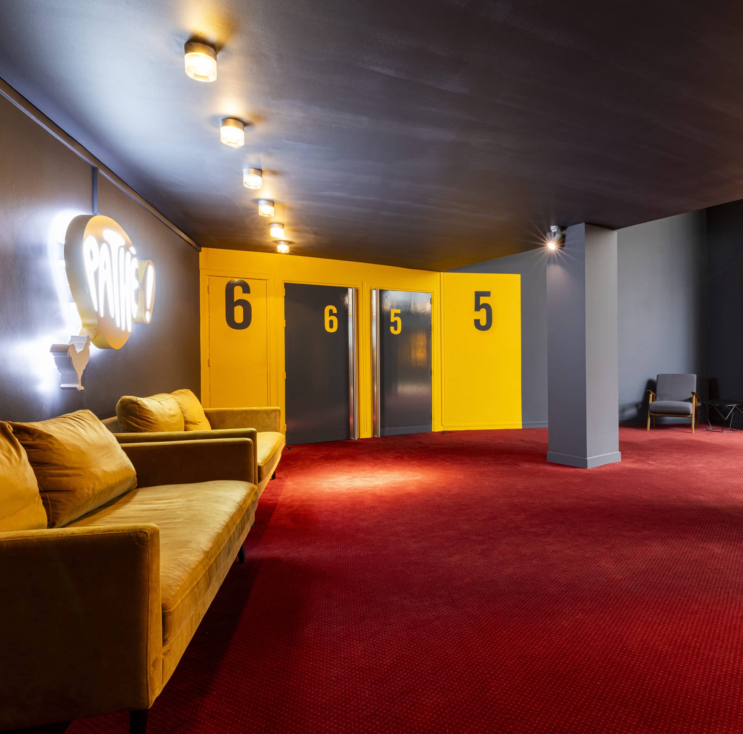 Espace de réception situé dans le hall du cinéma, éclairé par une lumière tamisée et aménagé avec des canapés et du mobilier de salon.