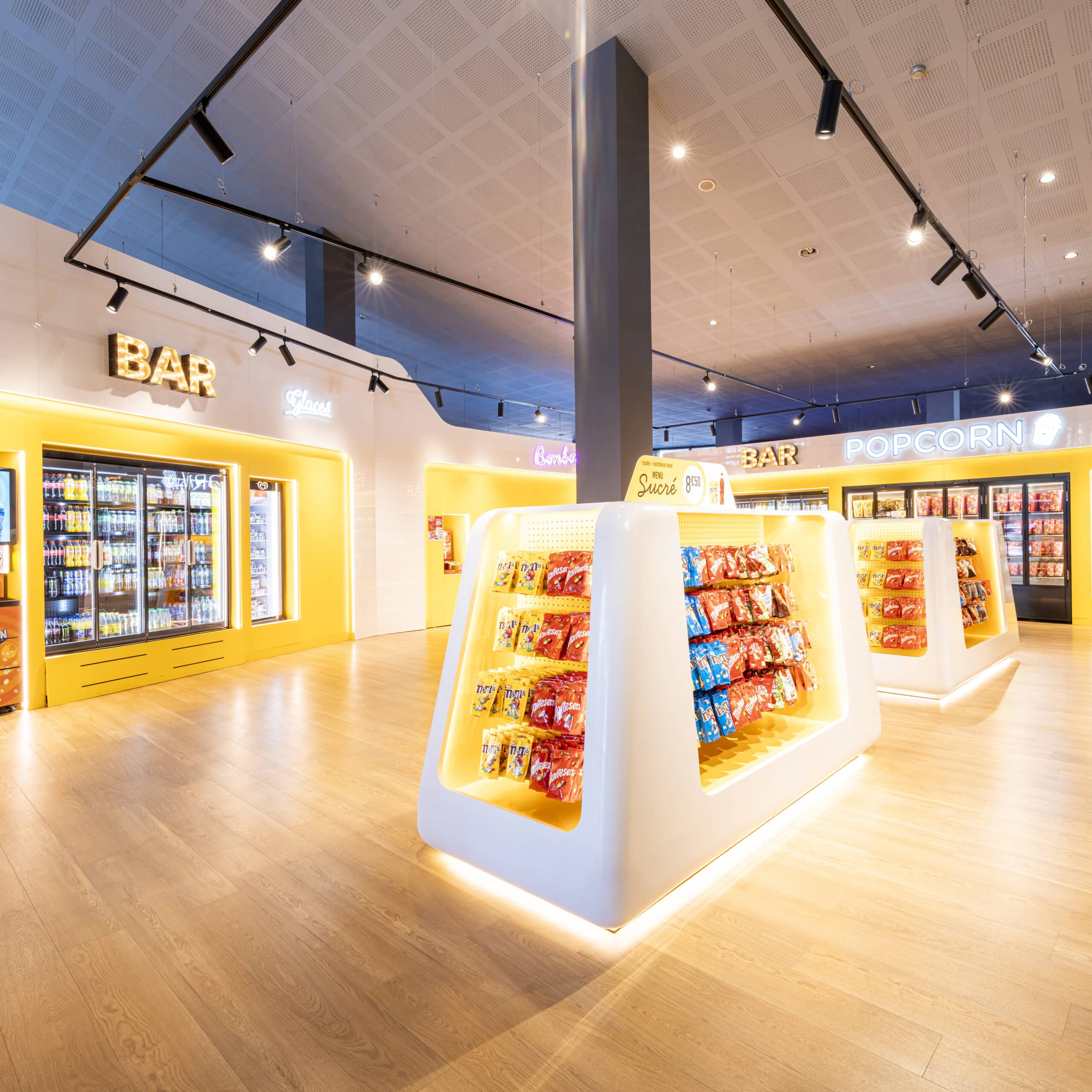 Espace confiserie du cinéma Pathé avec comptoir de pop-corn, distributeurs de boissons en libre-service et îlots de snacks et confiseries.