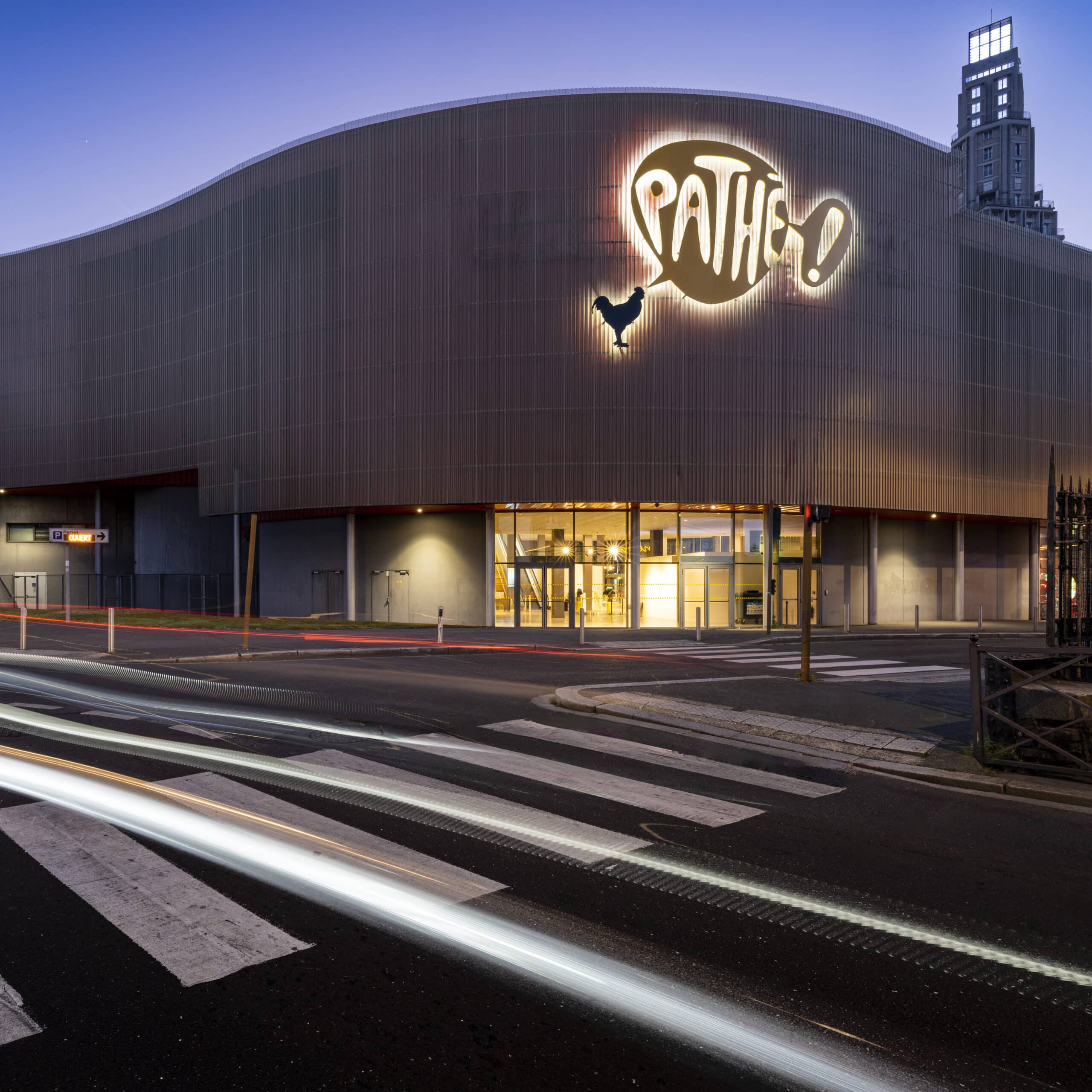 Façade extérieure du cinéma éclairée à la tombée de la nuit avec le logo Pathé mit en valeur.