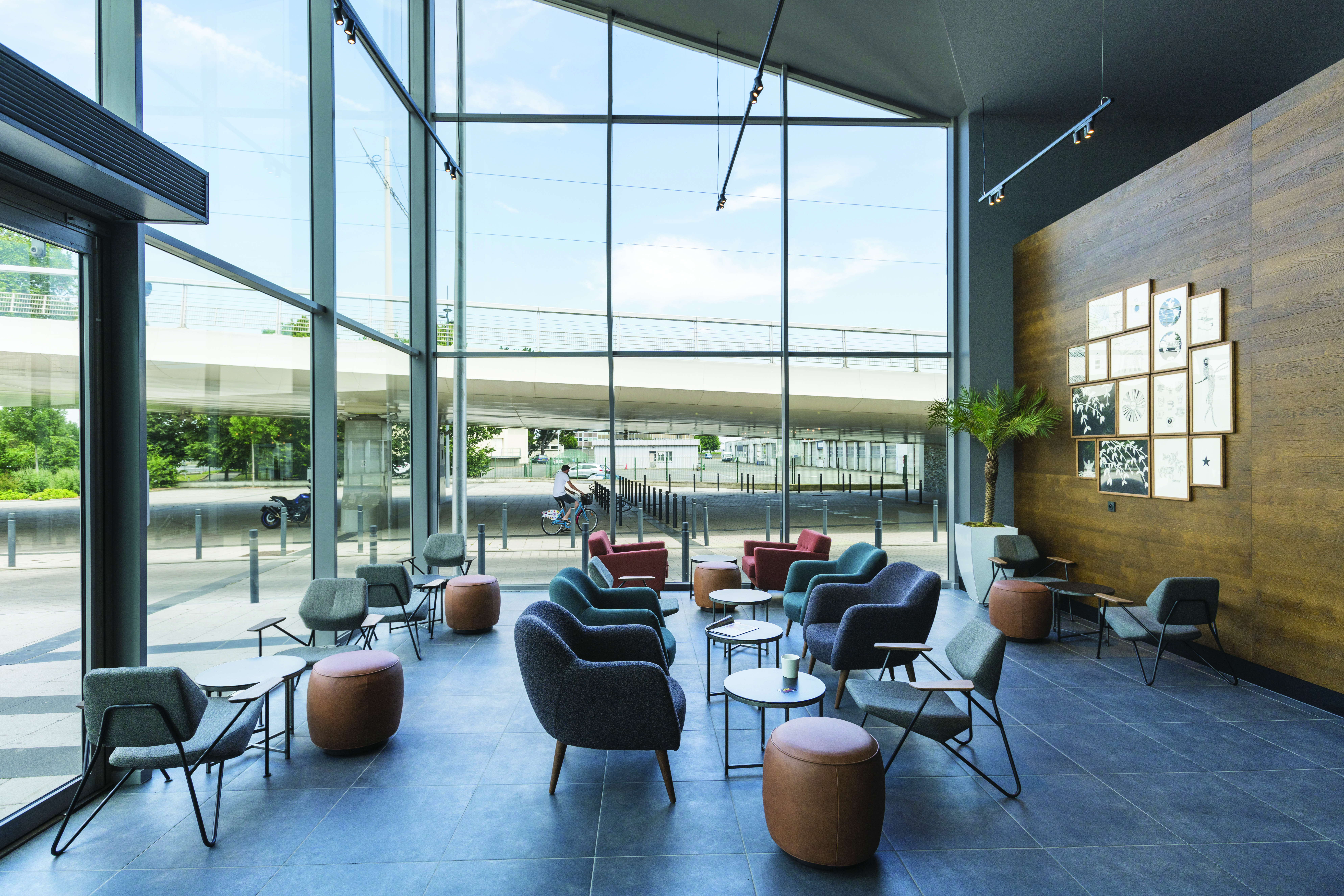 Espace lounge du cinéma avec larges baies vitrées, mobilier confortable et décorations murales en bois.