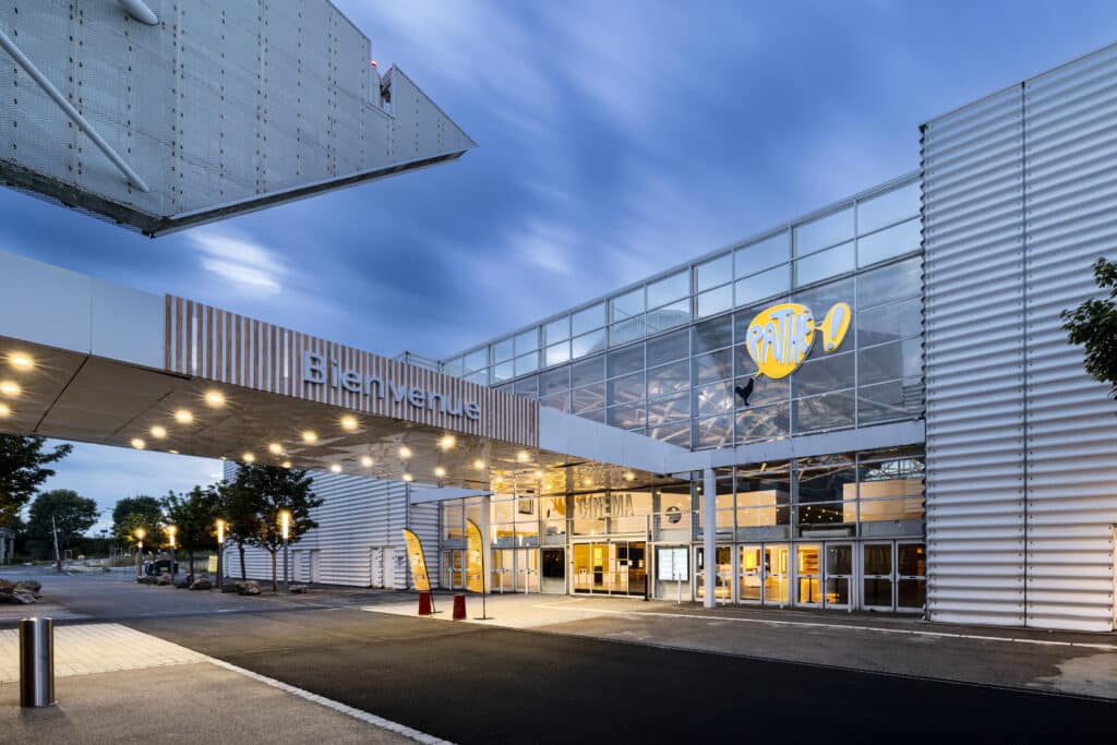Façade extérieure du cinéma éclairée à la tombée de la nuit avec le logo Pathé mit en valeur.