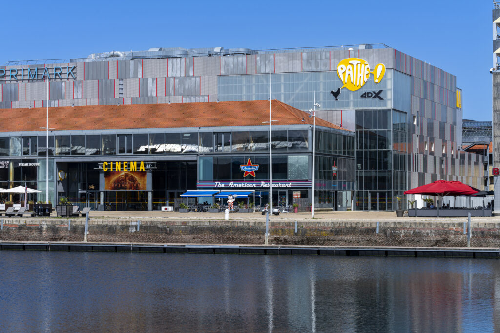 Façade extérieure du cinéma le long d'un point d'eau à la lumière du jour avec le logo Pathé apparent.