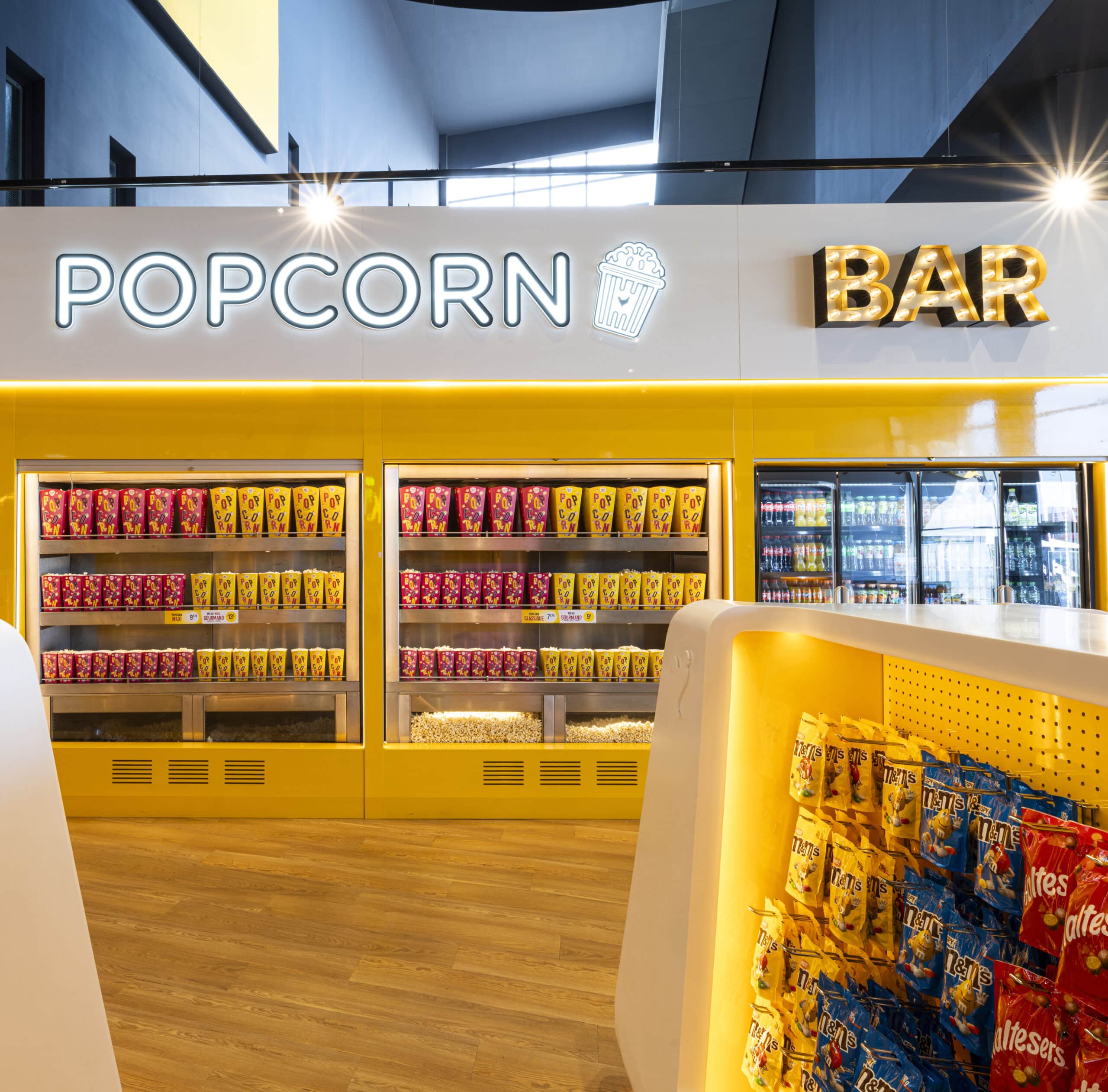Espace confiserie du cinéma Pathé avec comptoir de pop-corn, distributeurs de boissons en libre-service et îlots de snacks et confiseries.