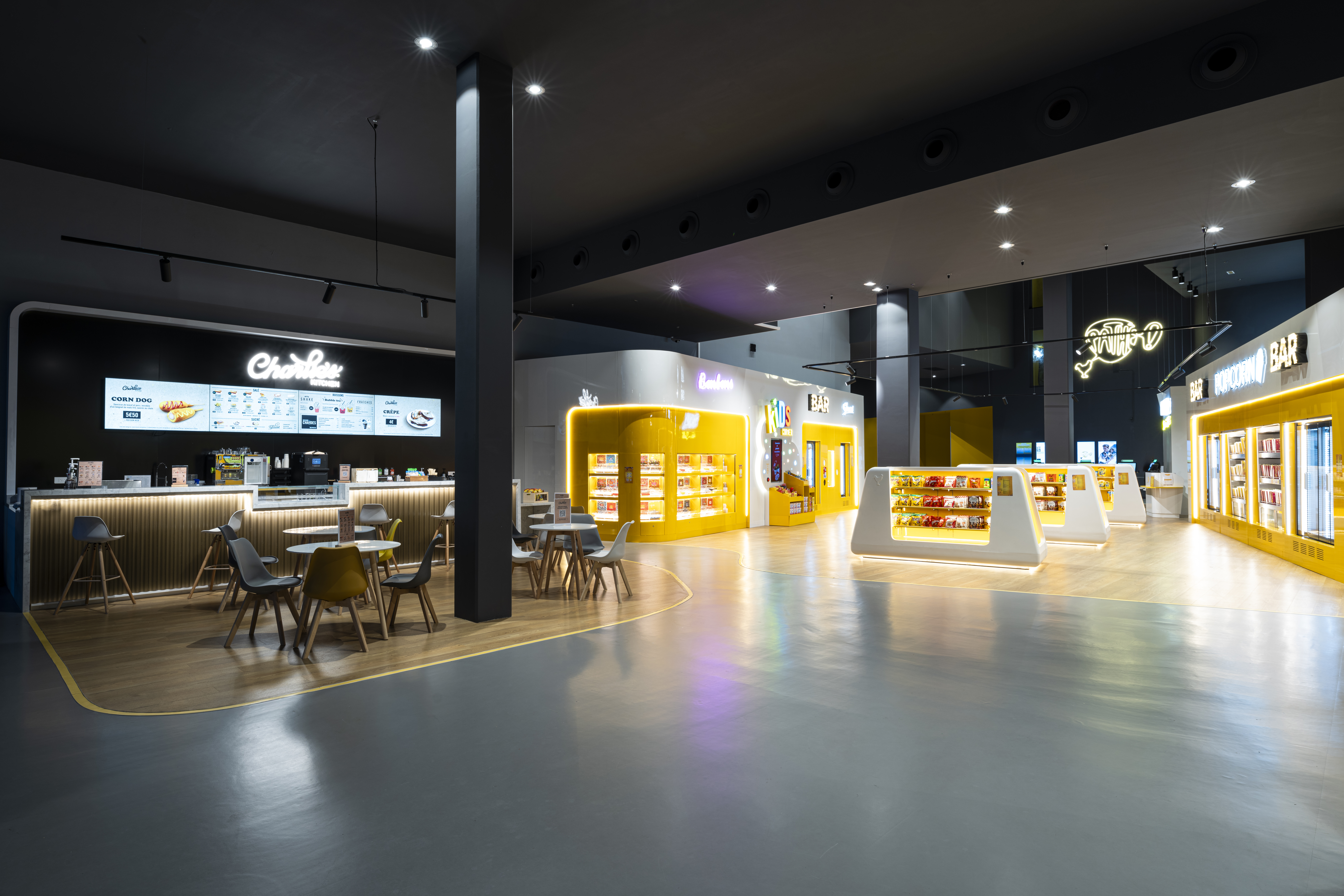 Hall de cinéma spacieux et moderne avec un bar lumineux proposant des confiseries, des bornes automatiques, et des indications vers les salles.