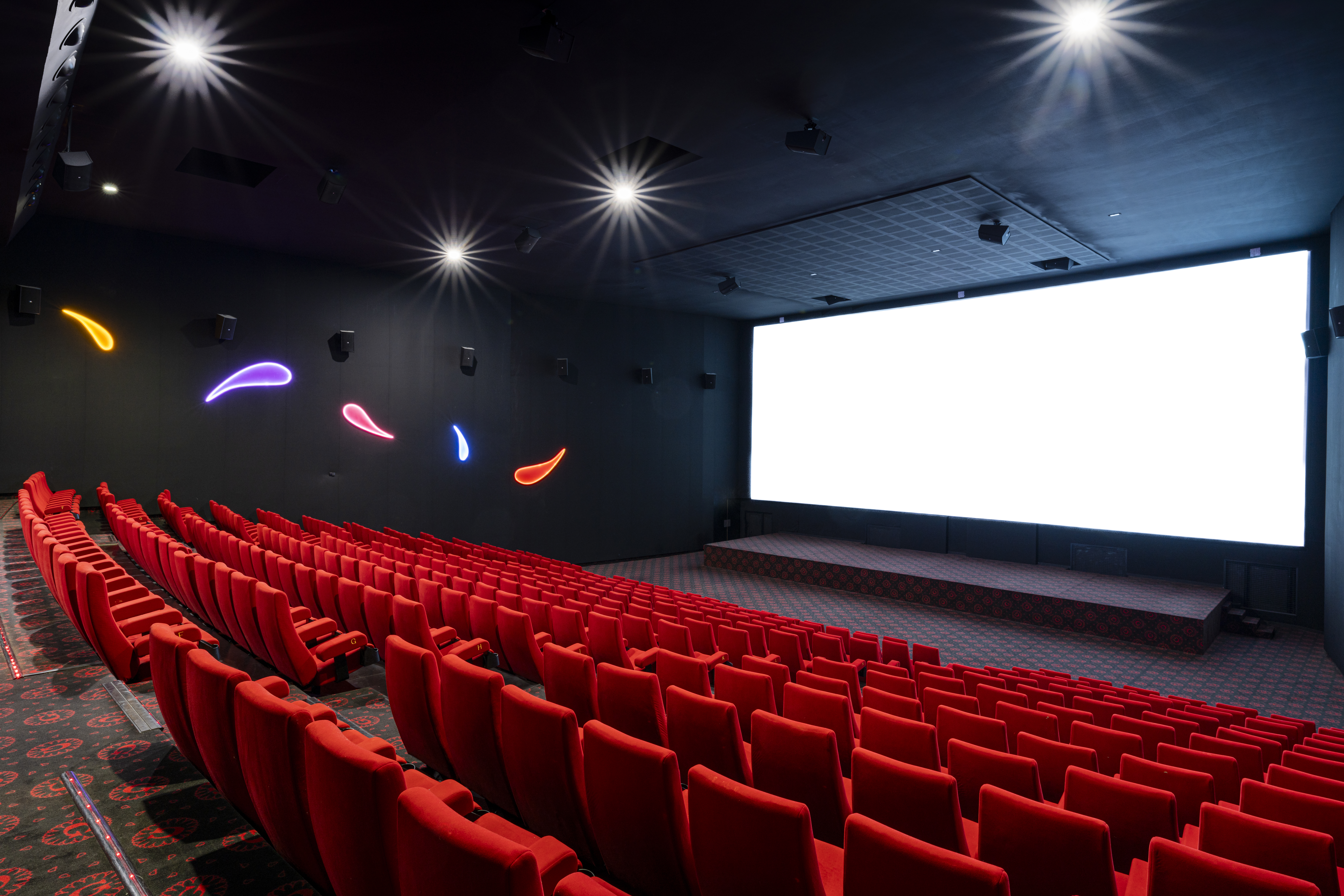 Vue depuis l’arrière d'une salle du cinéma Pathé avec ses rangées de fauteuils en velours rouges orientés vers l’écran.