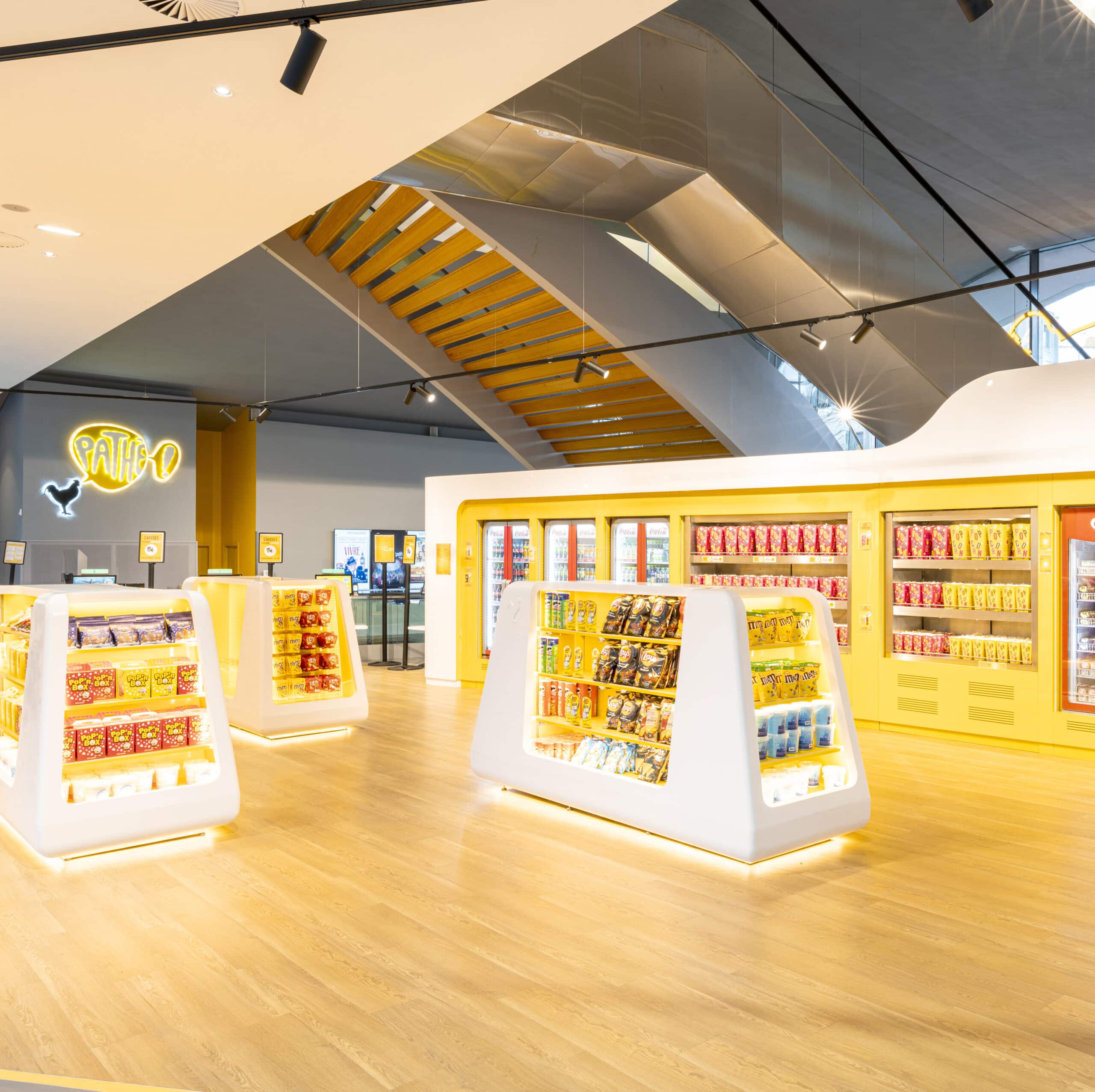 Espace confiserie du cinéma Pathé avec comptoir de pop-corn, distributeurs de boissons en libre-service et îlots de snacks et confiseries.