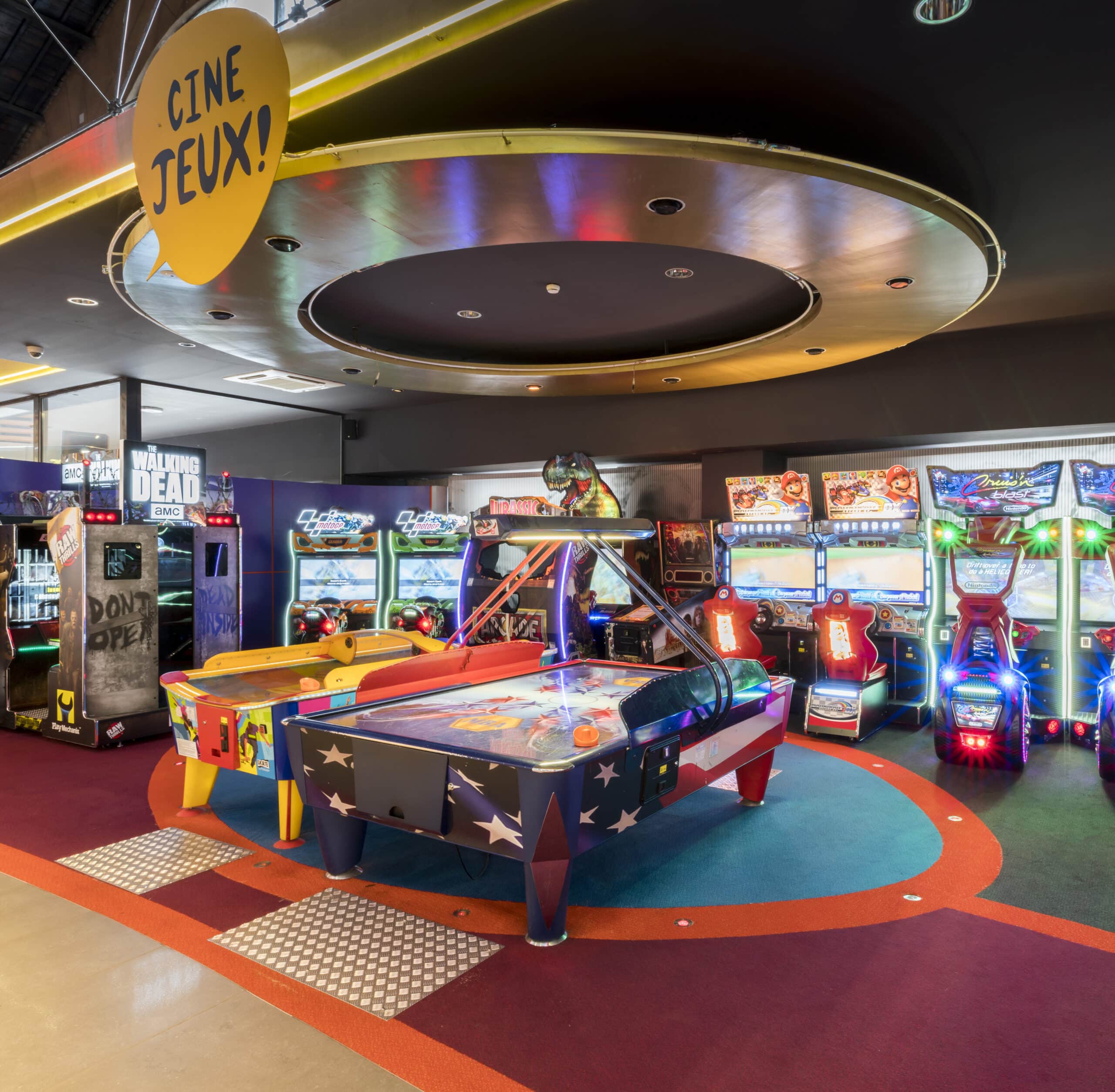 Espace Pathé Games avec différentes machines d’arcade et de jeux vidéo, éclairage néon coloré, ambiance moderne et ludique, proposant des jeux pour tous les âges dans un cadre convivial.