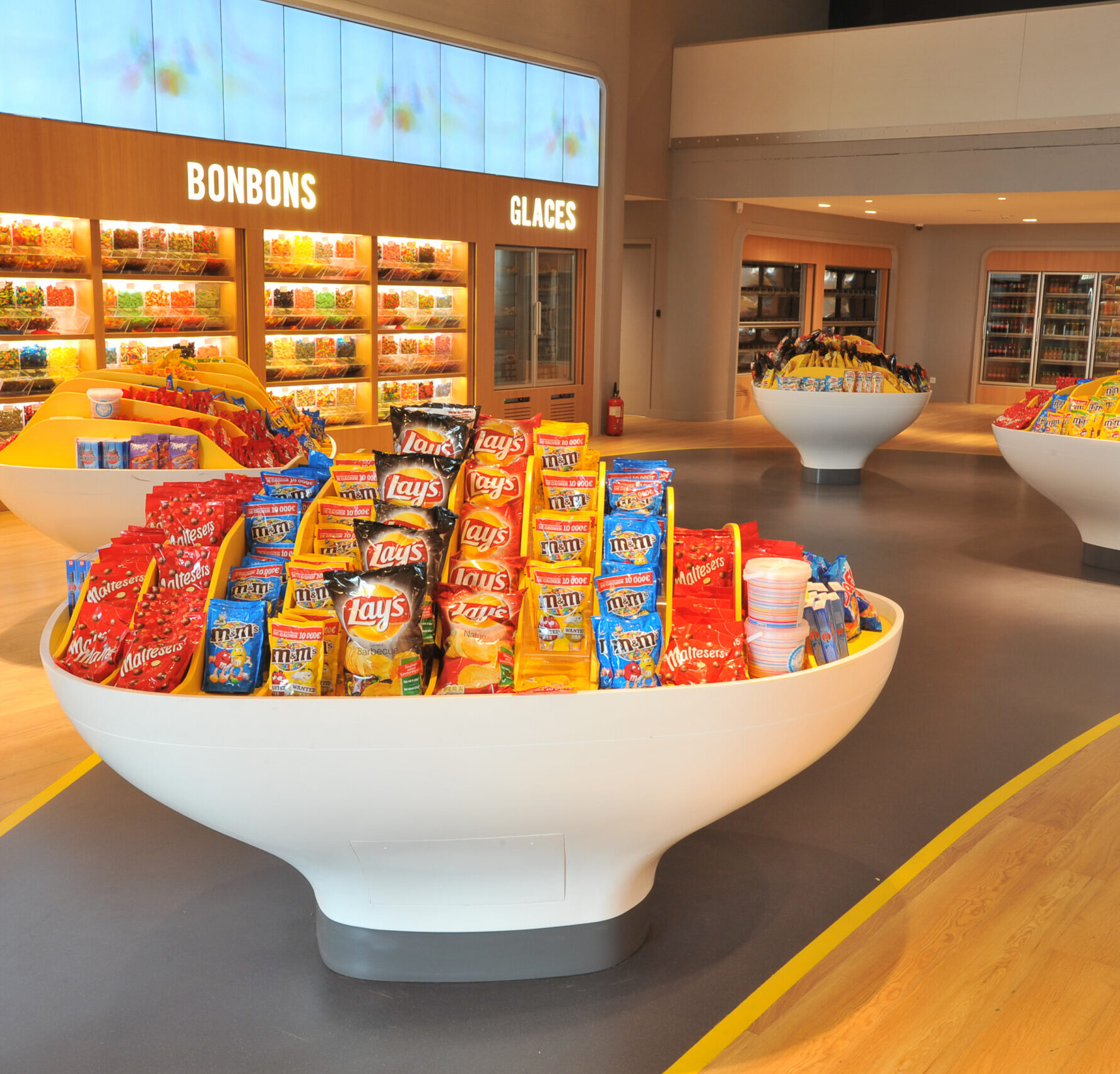 Espace confiserie du cinéma Pathé avec comptoir de pop-corn, distributeurs de boissons en libre-service et îlots de snacks et confiseries.