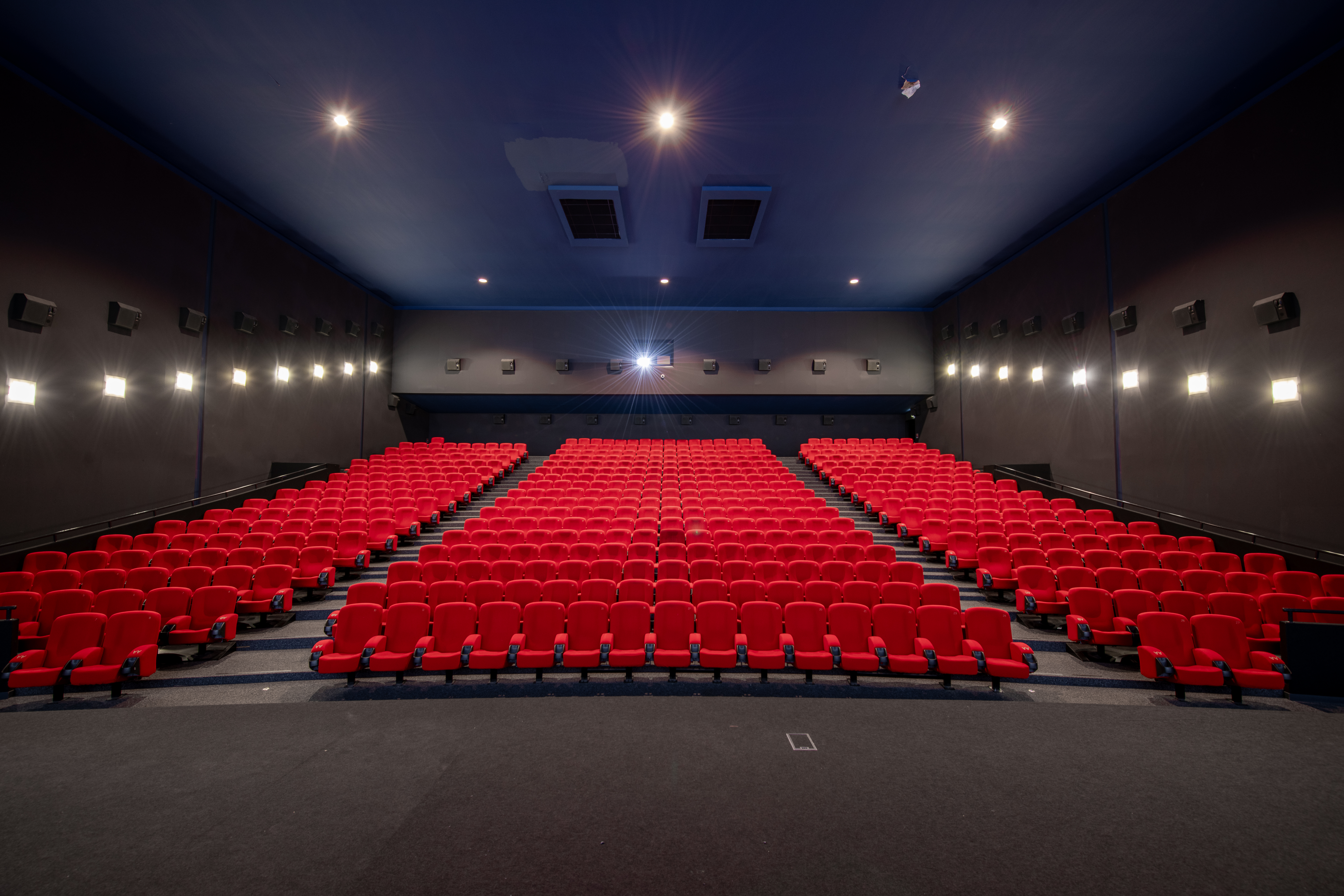 Vu d'ensemble de face d'une grande salle de cinéma Pathé avec ses fauteuils en velours rouge et ses spots lumineux qui éclairent la salle.