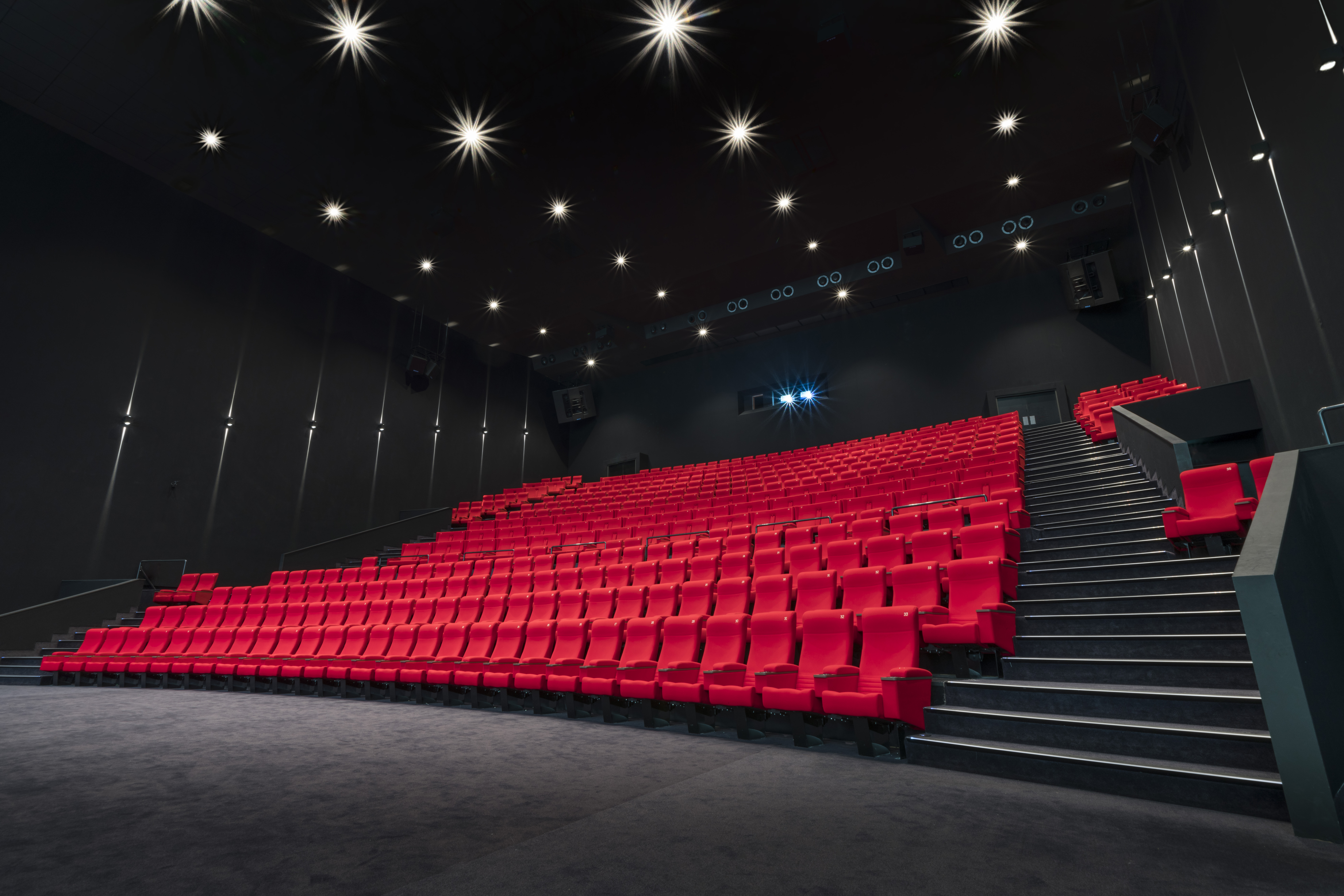 Vu d'ensemble de face d'une grande salle de cinéma Pathé avec ses fauteuils en velours rouge et ses spots lumineux qui éclairent la salle.