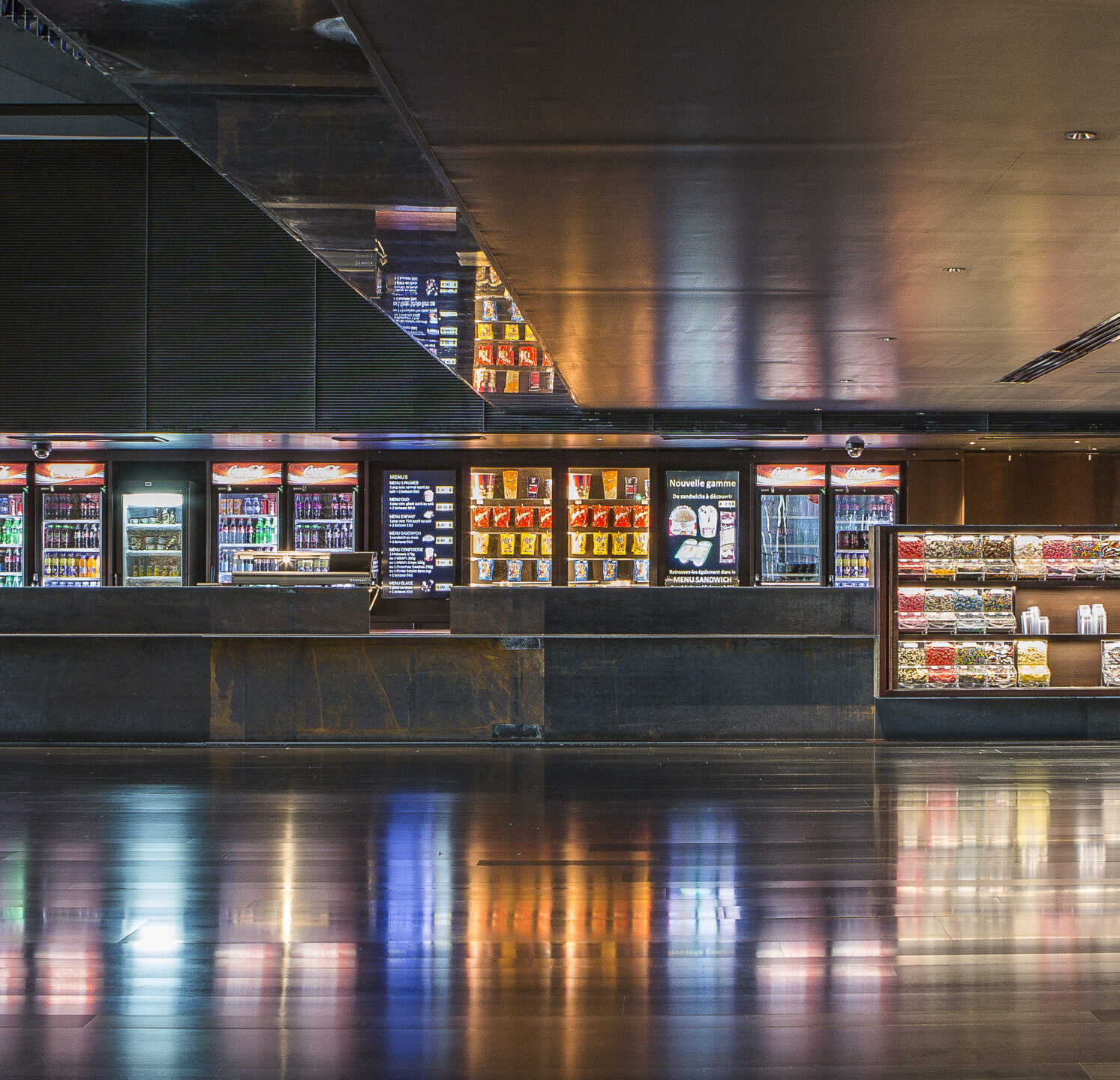Espace confiserie du cinéma Pathé avec comptoir de pop-corn, distributeurs de boissons en libre-service et îlots de snacks et confiseries.