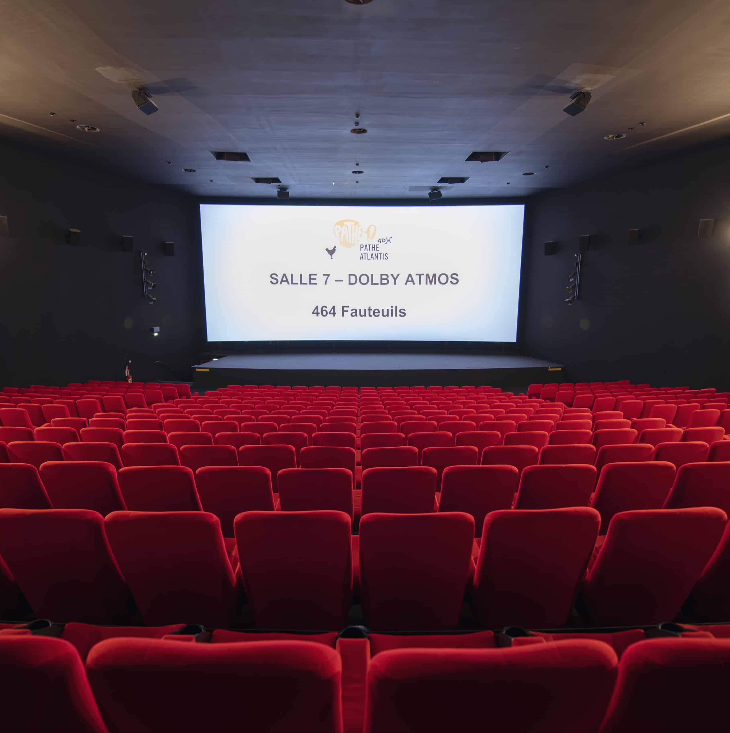 Vue depuis l’arrière de la salle 7 du cinéma Pathé Atlantis avec rangées de fauteuils en velours rouges orientés vers l’écran.