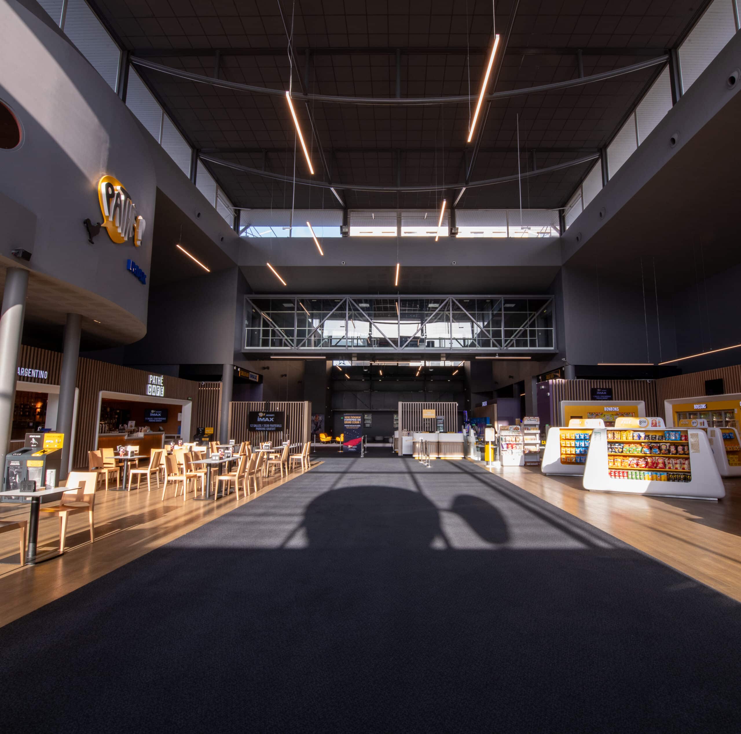 Grand hall du cinéma avec espaces de restauration, vitrines de confiseries et design moderne sous un éclairage naturel.