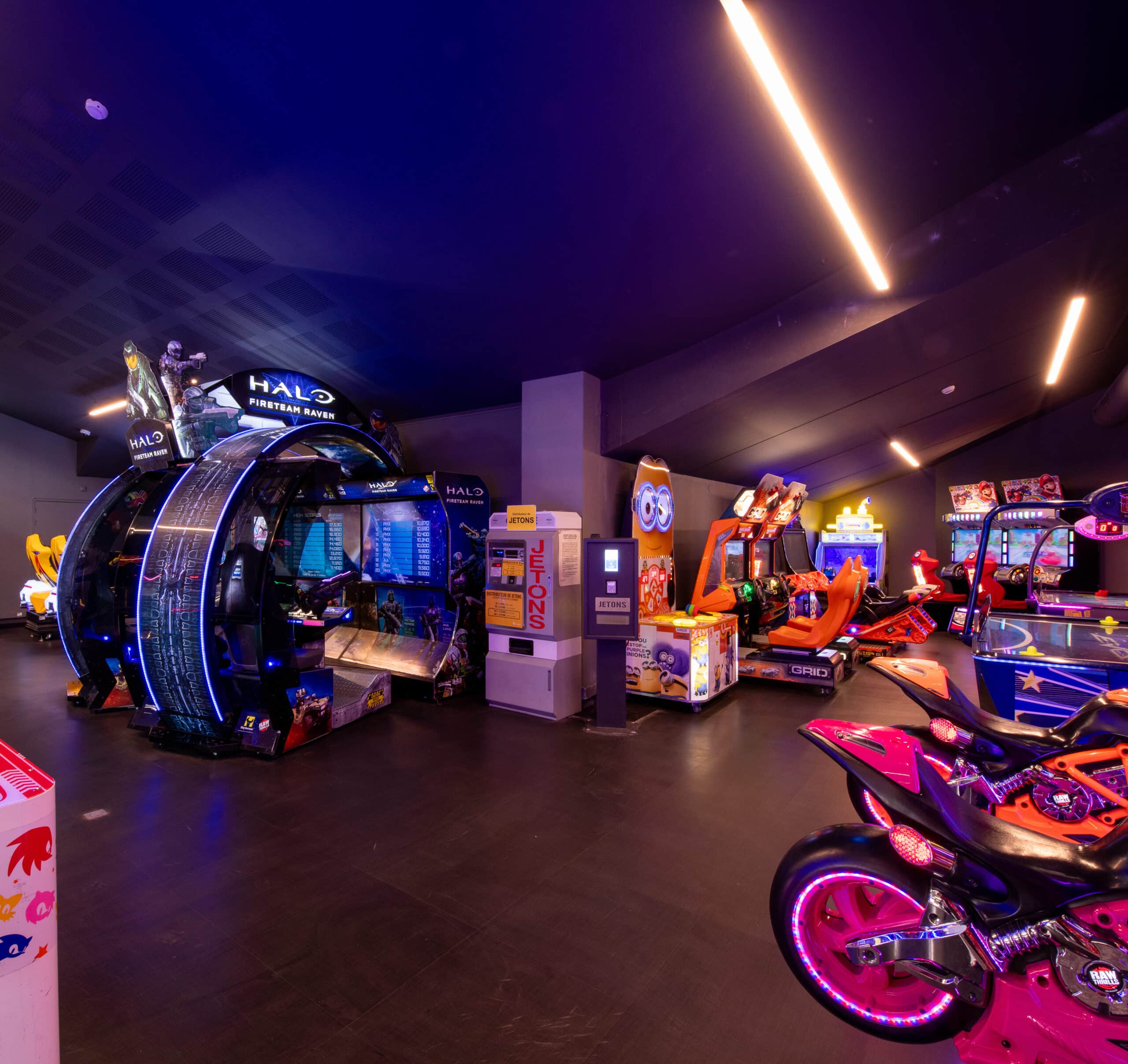Espace Pathé Games avec différentes machines d’arcade et de jeux vidéo, éclairage néon coloré, ambiance moderne et ludique, proposant des jeux pour tous les âges dans un cadre convivial.