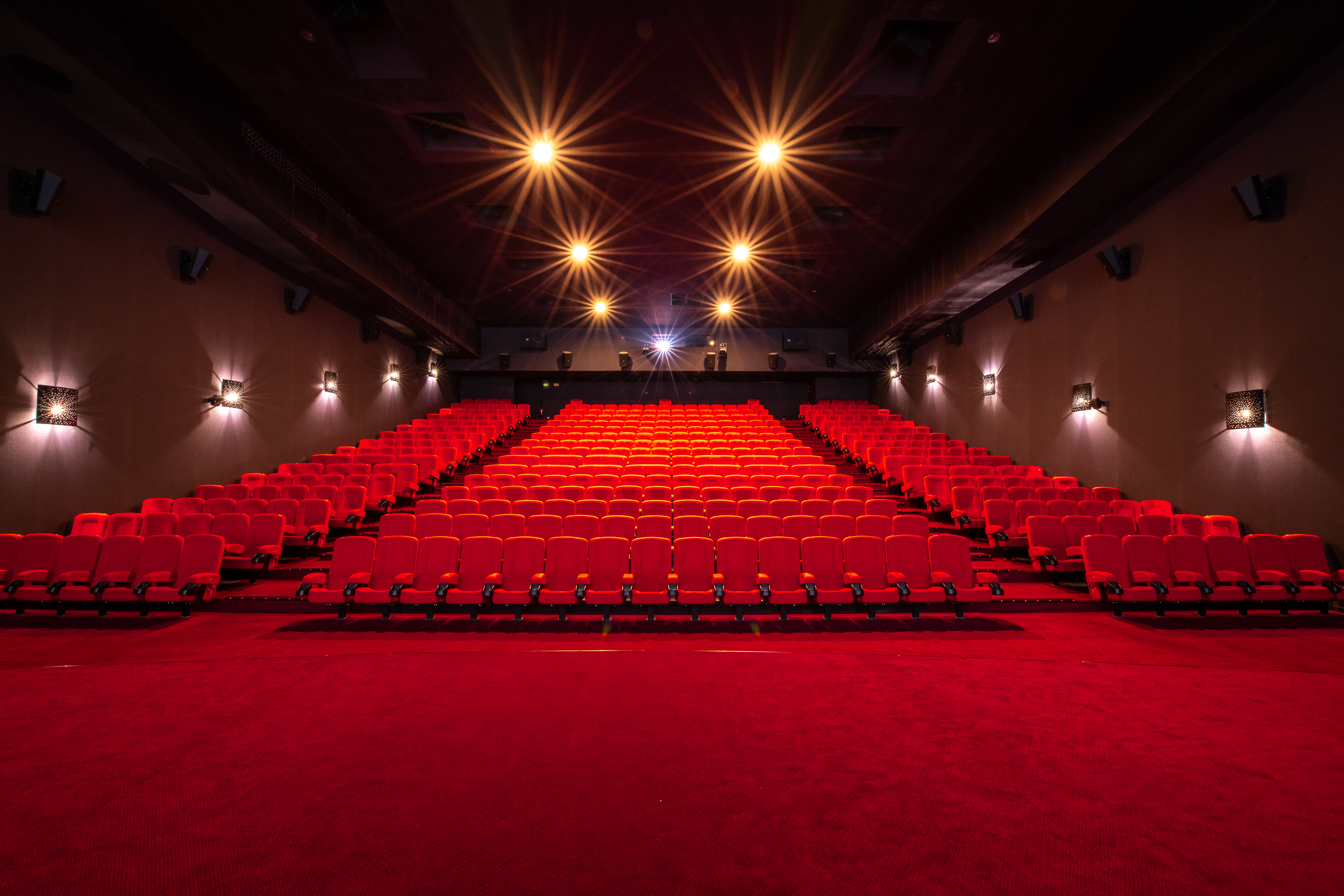 Vu d'ensemble de face d'une salle de cinéma Pathé avec ses fauteuils en velours rouge et sa moquette rouge au sol.