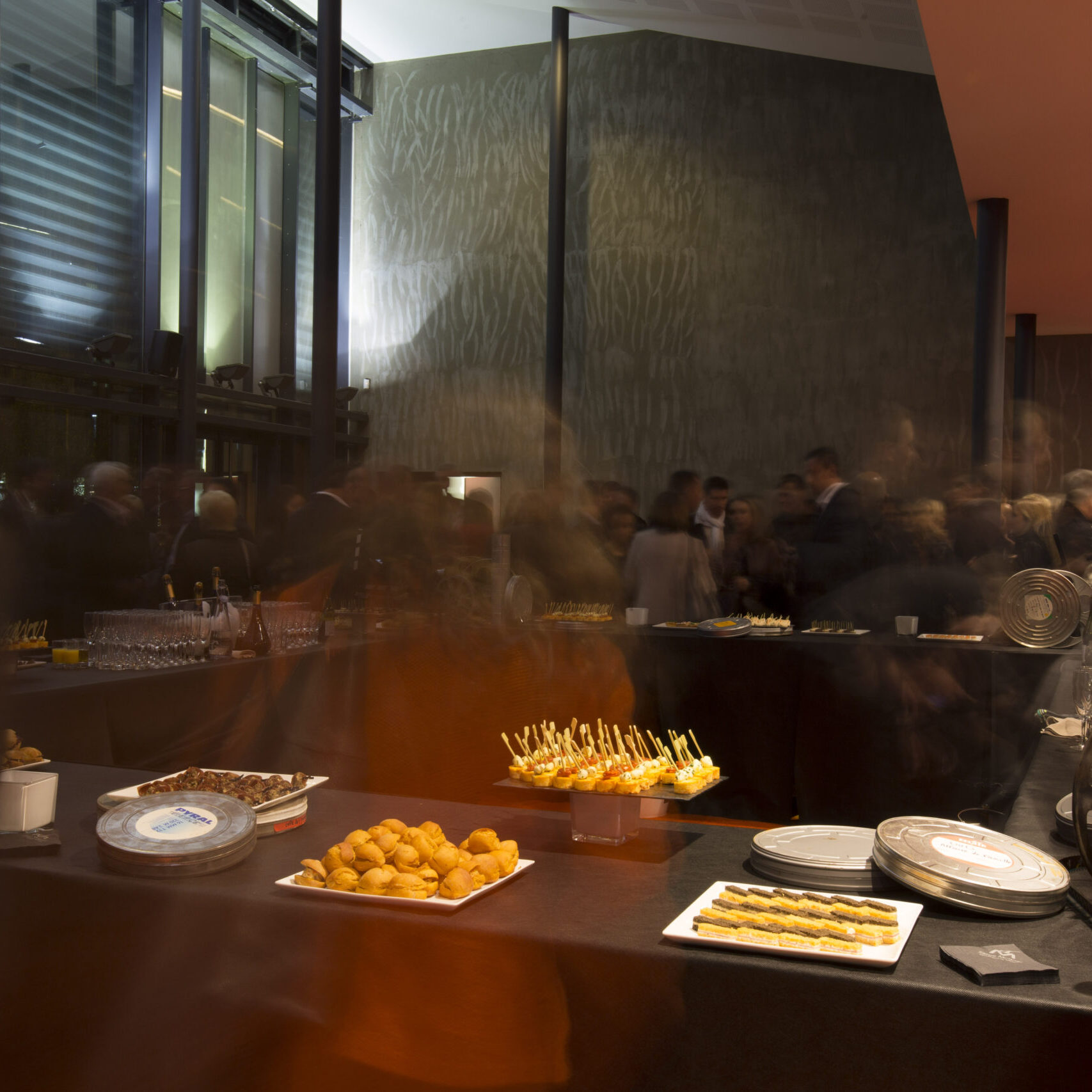 Salle de réception avec buffet élégant proposant divers plats et amuse-bouches. Les grandes baies vitrées offrent une ambiance lumineuse et moderne.