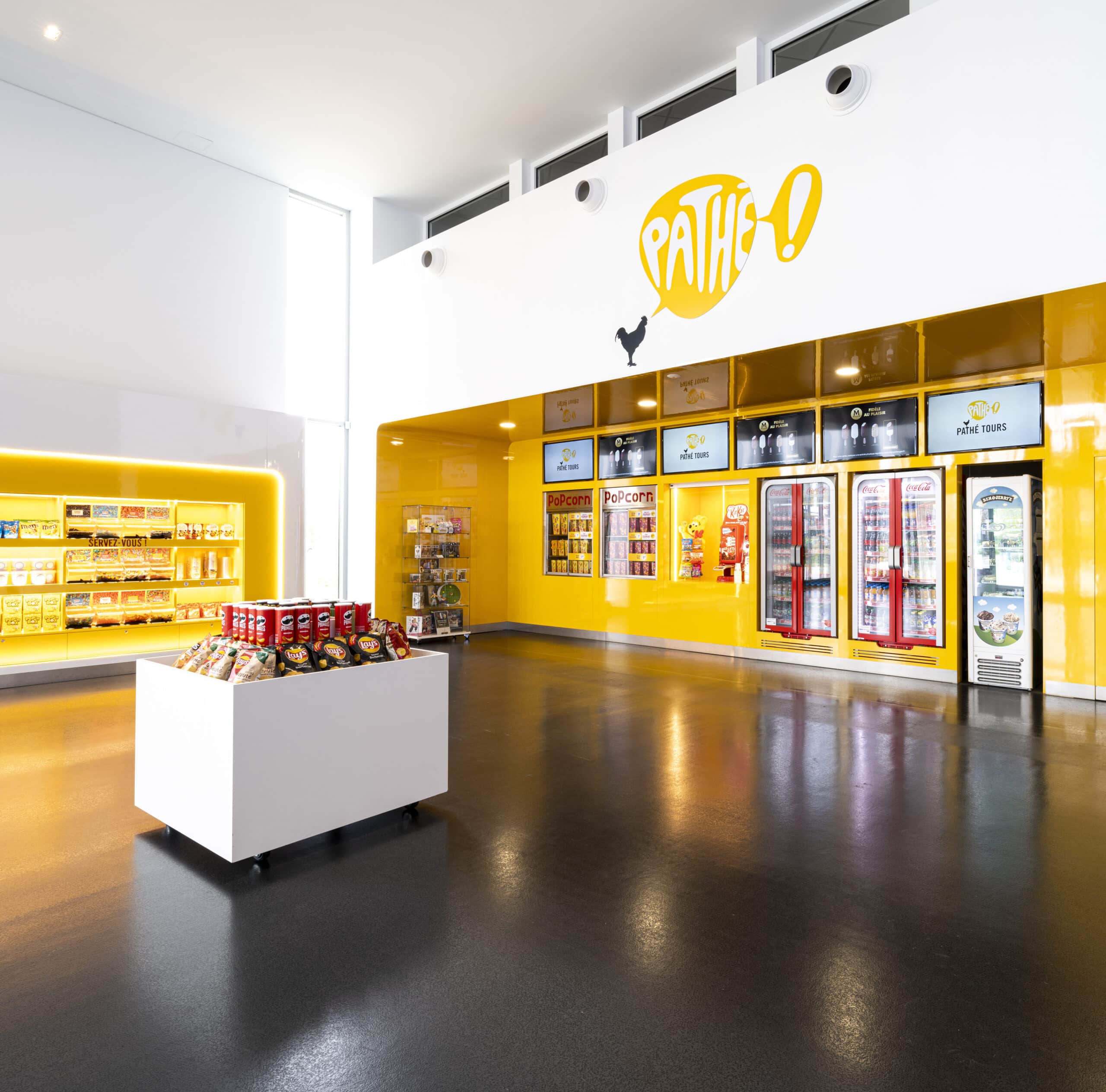 Espace confiserie du cinéma Pathé avec comptoir de pop-corn, distributeurs de boissons en libre-service et îlots de snacks et confiseries.