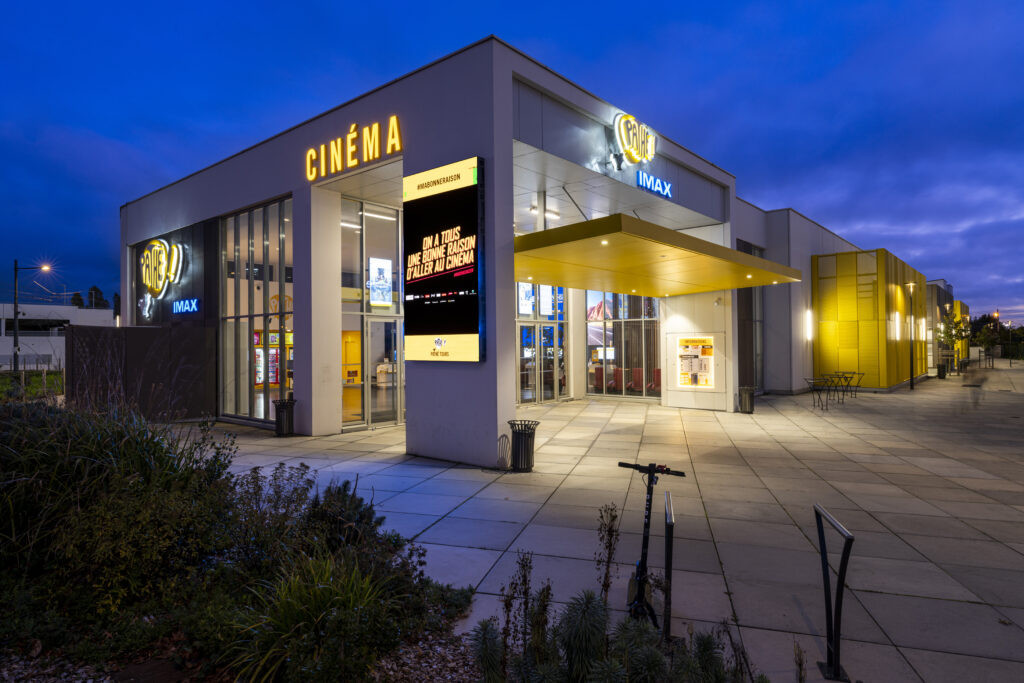 Façade extérieure du cinéma éclairée à la tombée de la nuit avec le logo Pathé mit en valeur.