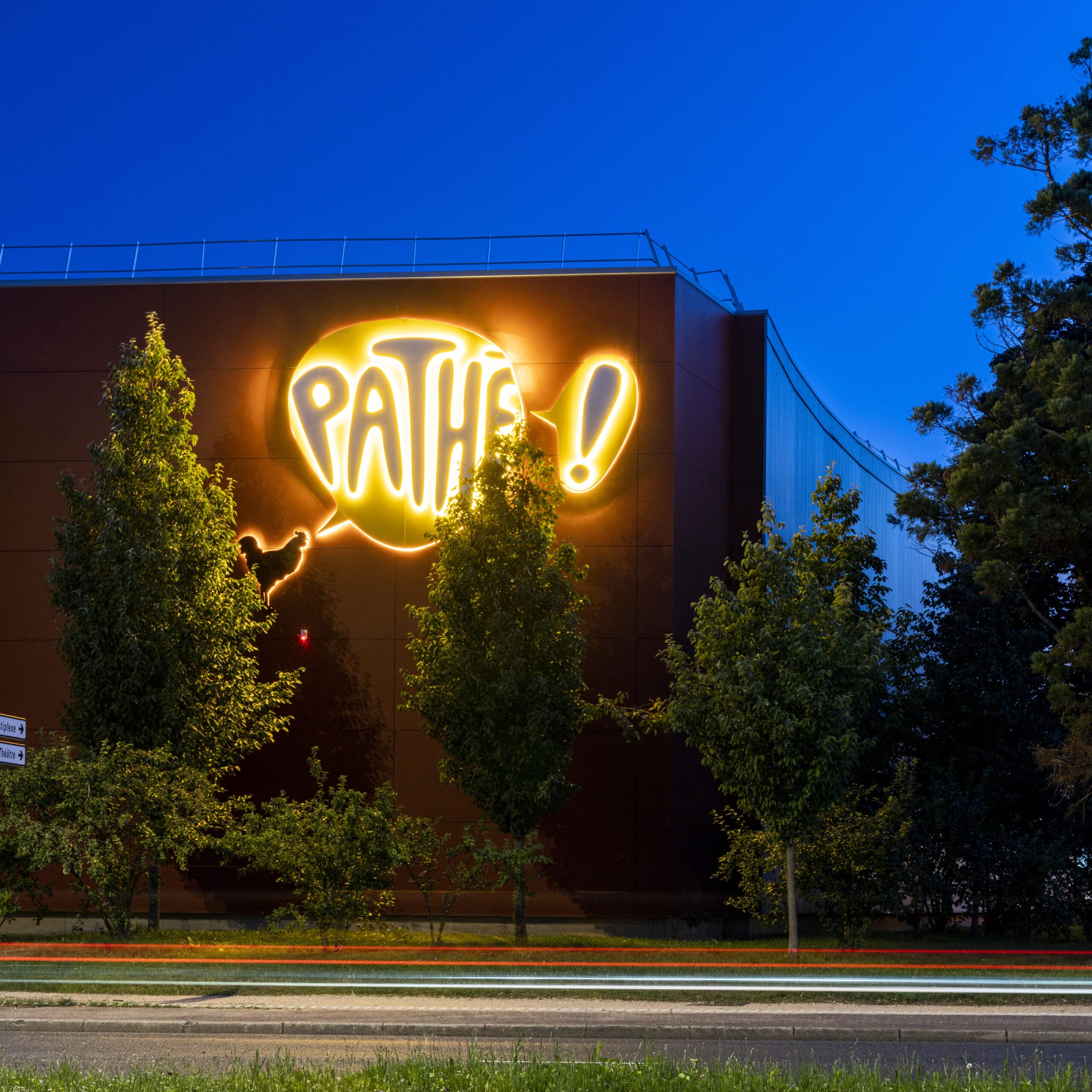 Façade extérieure du cinéma éclairée à la tombée de la nuit avec le logo Pathé en lumière jaune.