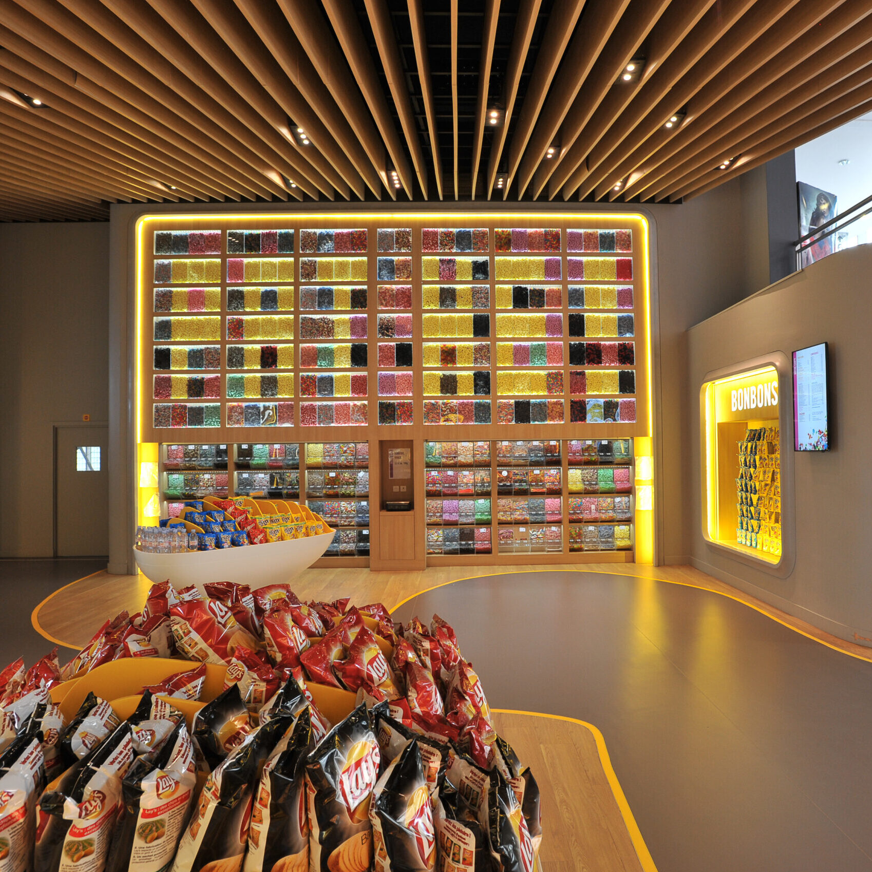 Espace confiserie du cinéma Pathé avec un mur de bonbons, distributeurs de boissons en libre-service et îlots de snacks et confiseries.